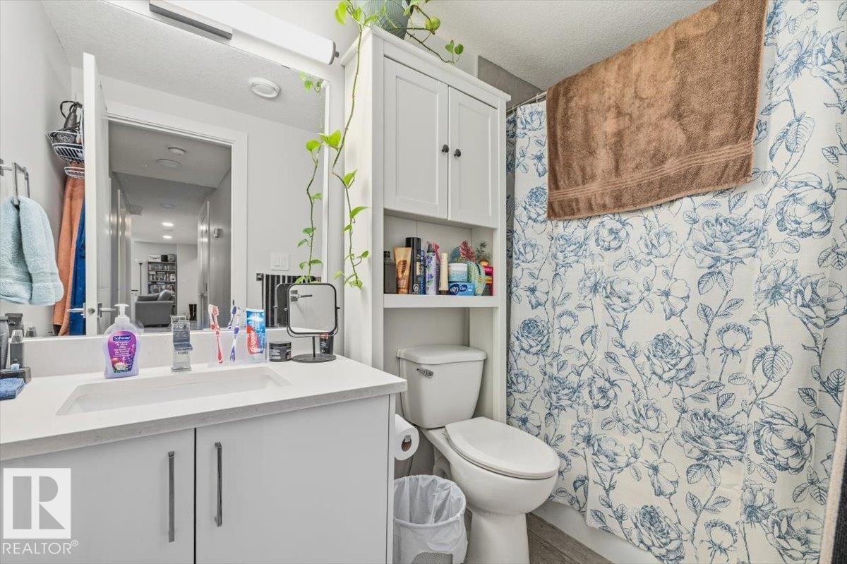 Bathroom featuring a white vanity with integrated sink, a rectangular wall mirror, a built-in storage cabinet, and a white toilet - 9933 79 Street, Edmonton, AB - Indoor Photo Showing Bathroom