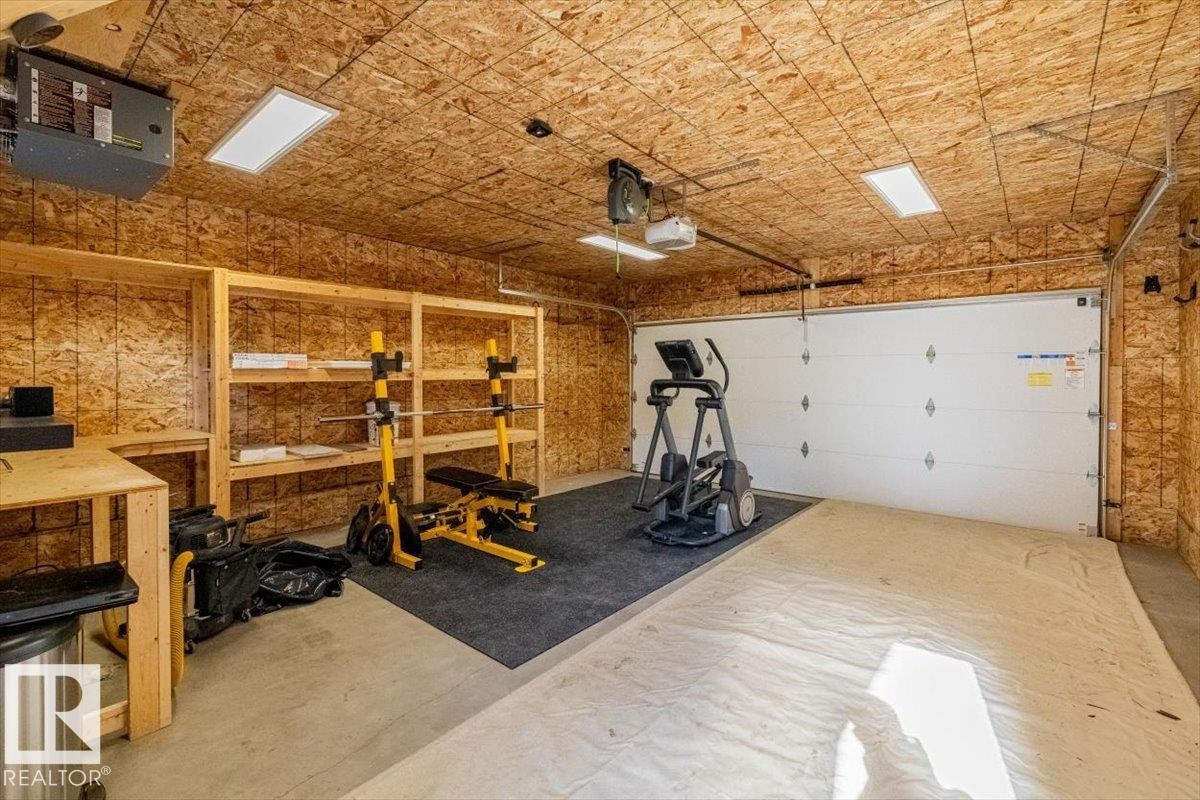 Garage space featuring a white sectional garage door, exposed OSB walls and ceiling, and a concrete floor - 9933 79 Street, Edmonton, AB - Indoor Photo Showing Garage