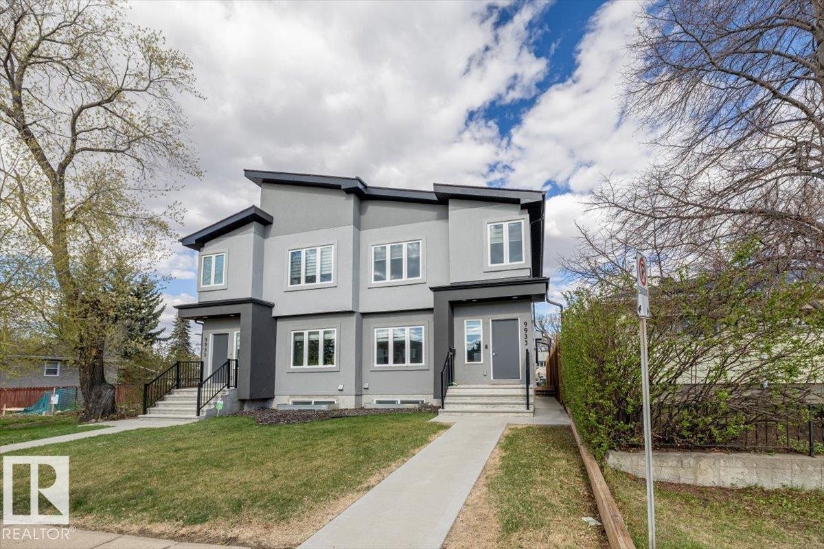 Modern duplex exterior featuring a multi-tone gray facade, white window frames, a dark gray main entry door, and black exterior railings - 9933 79 Street, Edmonton, AB - Outdoor With Facade