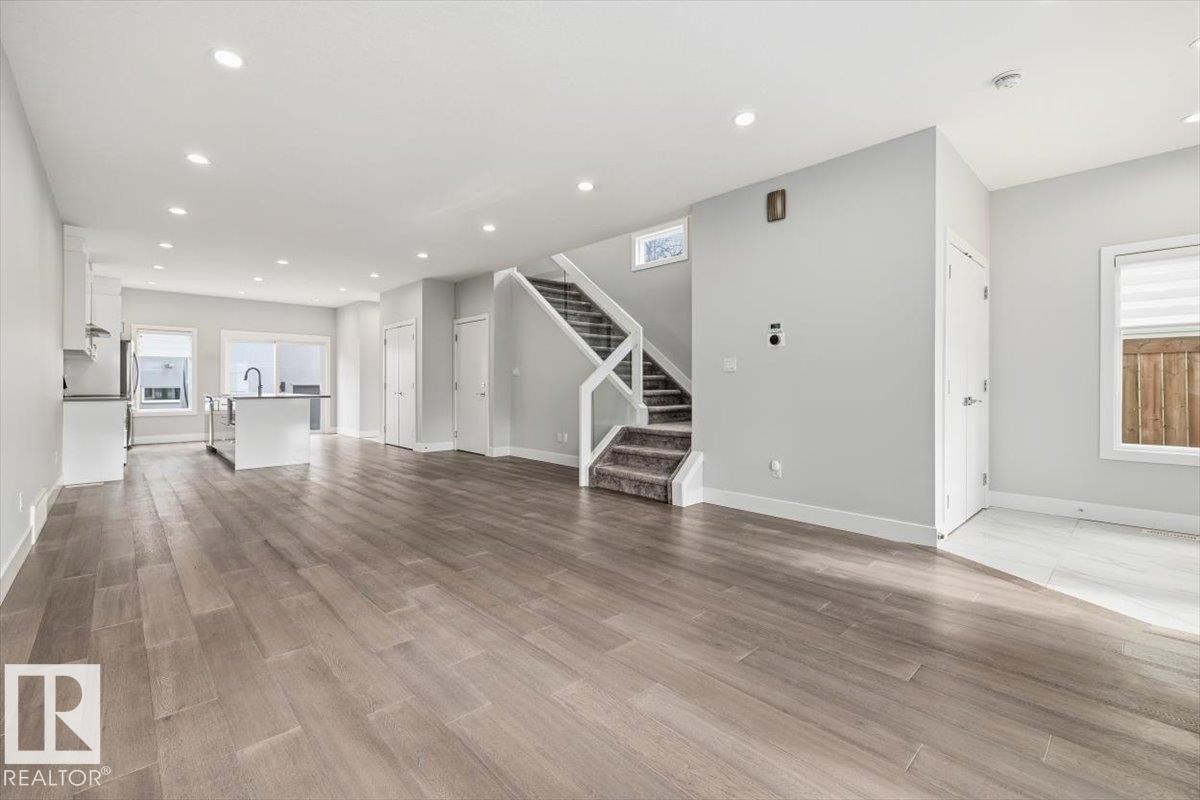 Spacious open-concept interior featuring light gray walls, recessed lighting, and wood-finish flooring - 9933 79 Street, Edmonton, AB - Indoor