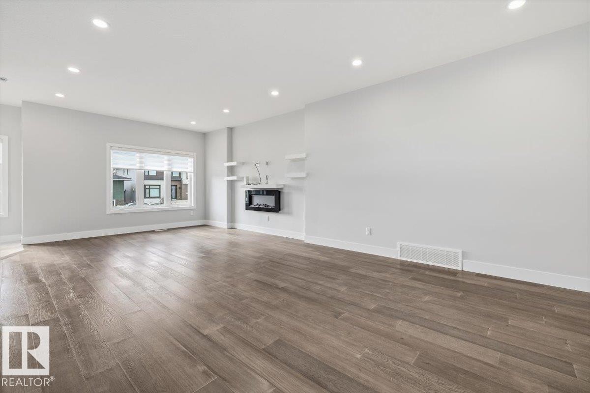 Spacious room featuring wood-finish flooring, recessed lighting, a modern wall-mounted fireplace, and multiple windows with blinds - 9933 79 Street, Edmonton, AB - Indoor Photo Showing Living Room With Fireplace