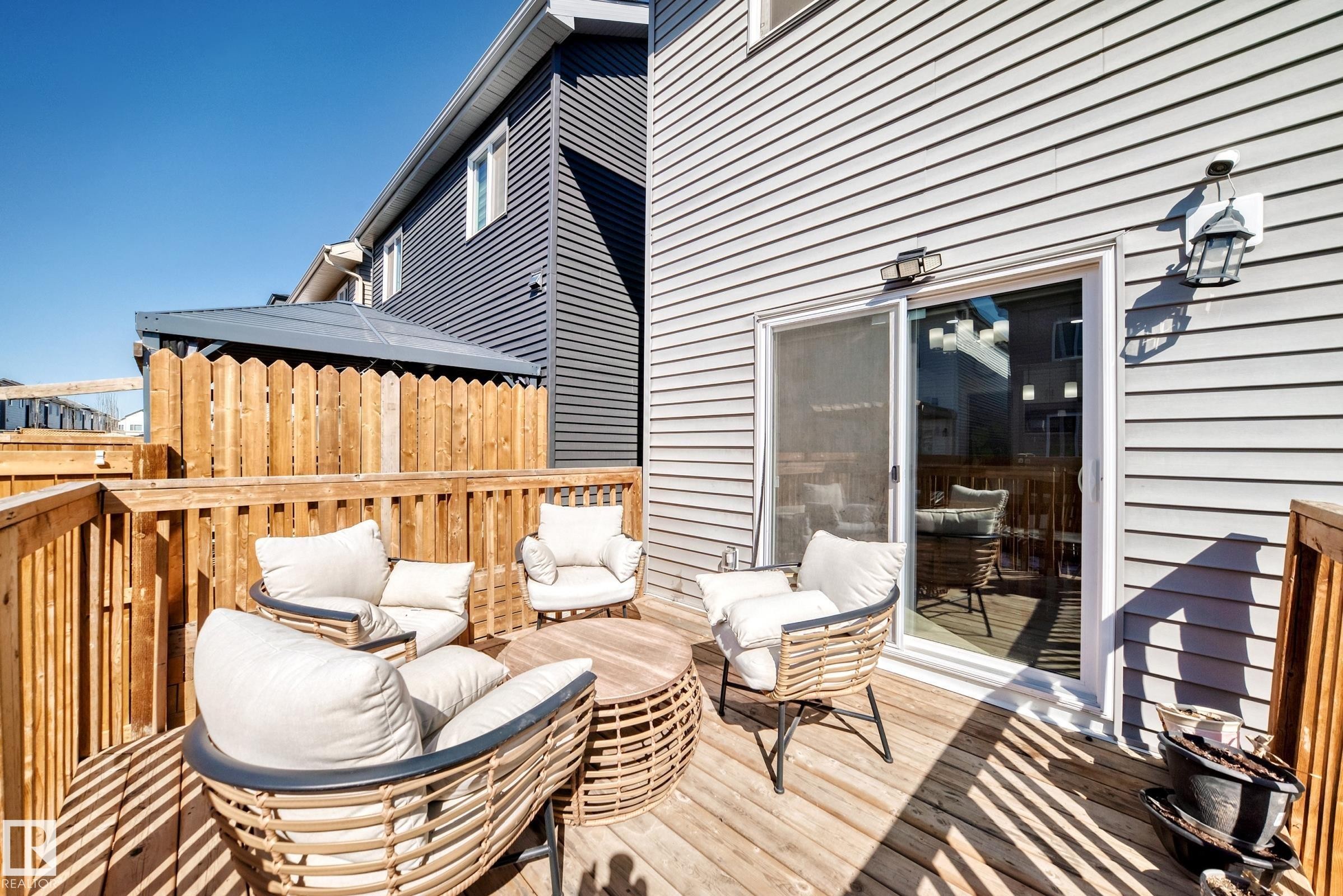 Spacious wood deck featuring a natural wood privacy fence, light gray horizontal siding, and a sliding glass door with an exterior wall lantern - 19635 29 Avenue, Edmonton, AB - Outdoor With Deck Patio Veranda