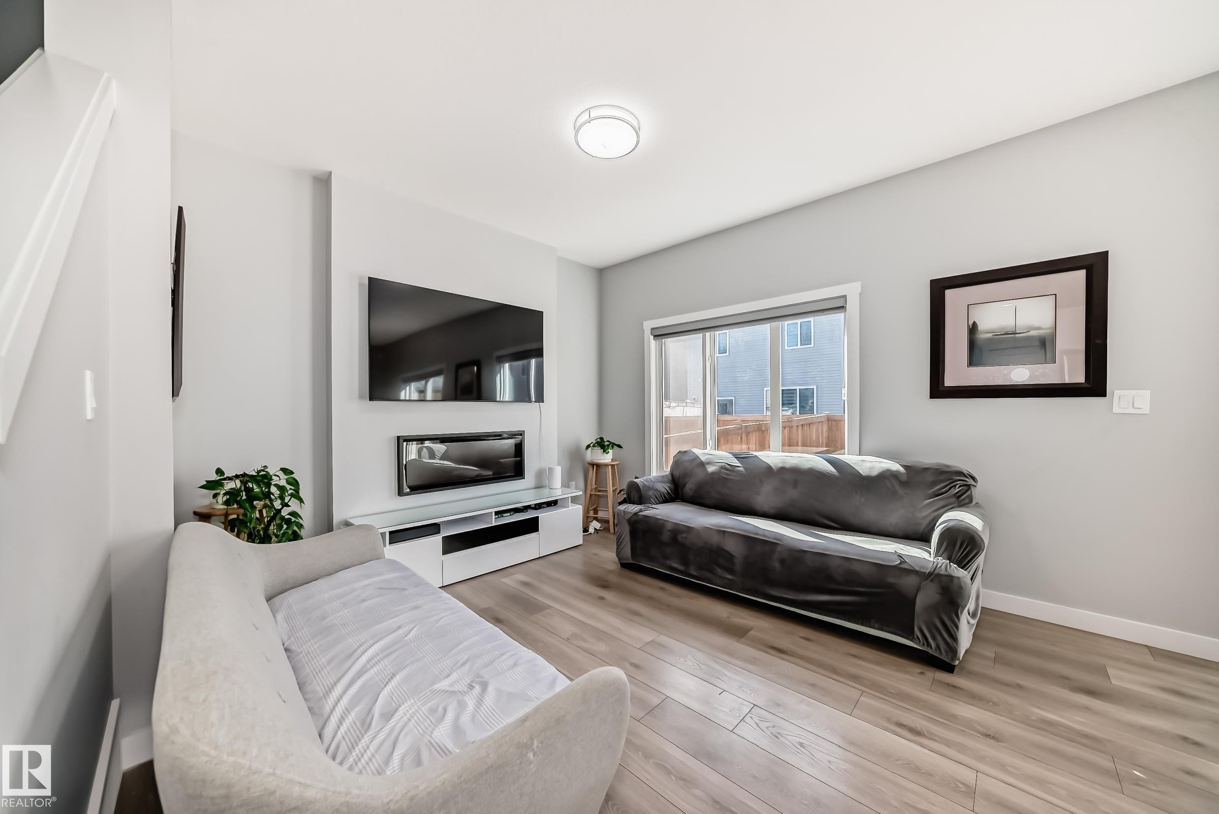 Living area featuring wood-finish flooring, light gray wall paint, and a sliding glass door - 19635 29 Avenue, Edmonton, AB - Indoor Photo Showing Living Room With Fireplace