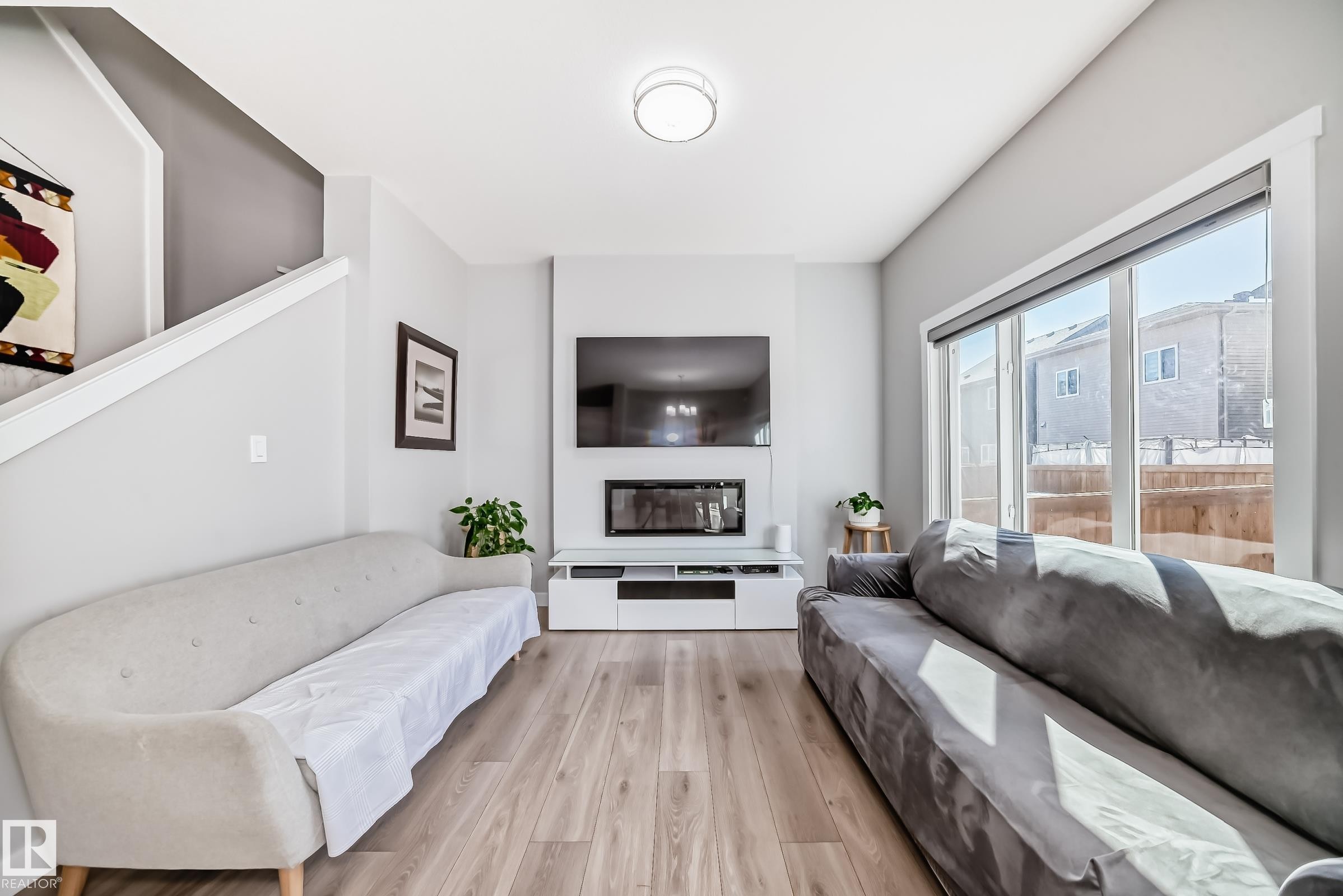 Living area featuring wood-finish flooring, a contemporary fireplace with a television mounted above, and a large sliding glass door - 19635 29 Avenue, Edmonton, AB - Indoor Photo Showing Living Room With Fireplace