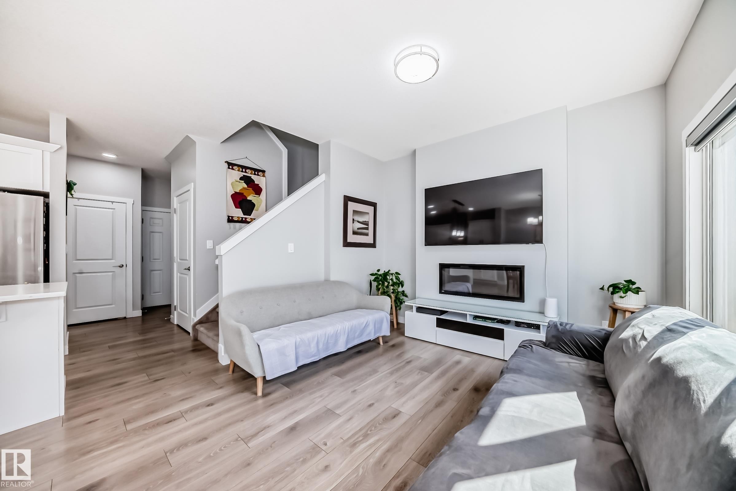 Open-concept living space featuring light wood-finish flooring, a contemporary electric fireplace, and a built-in media console - 19635 29 Avenue, Edmonton, AB - Indoor Photo Showing Living Room With Fireplace