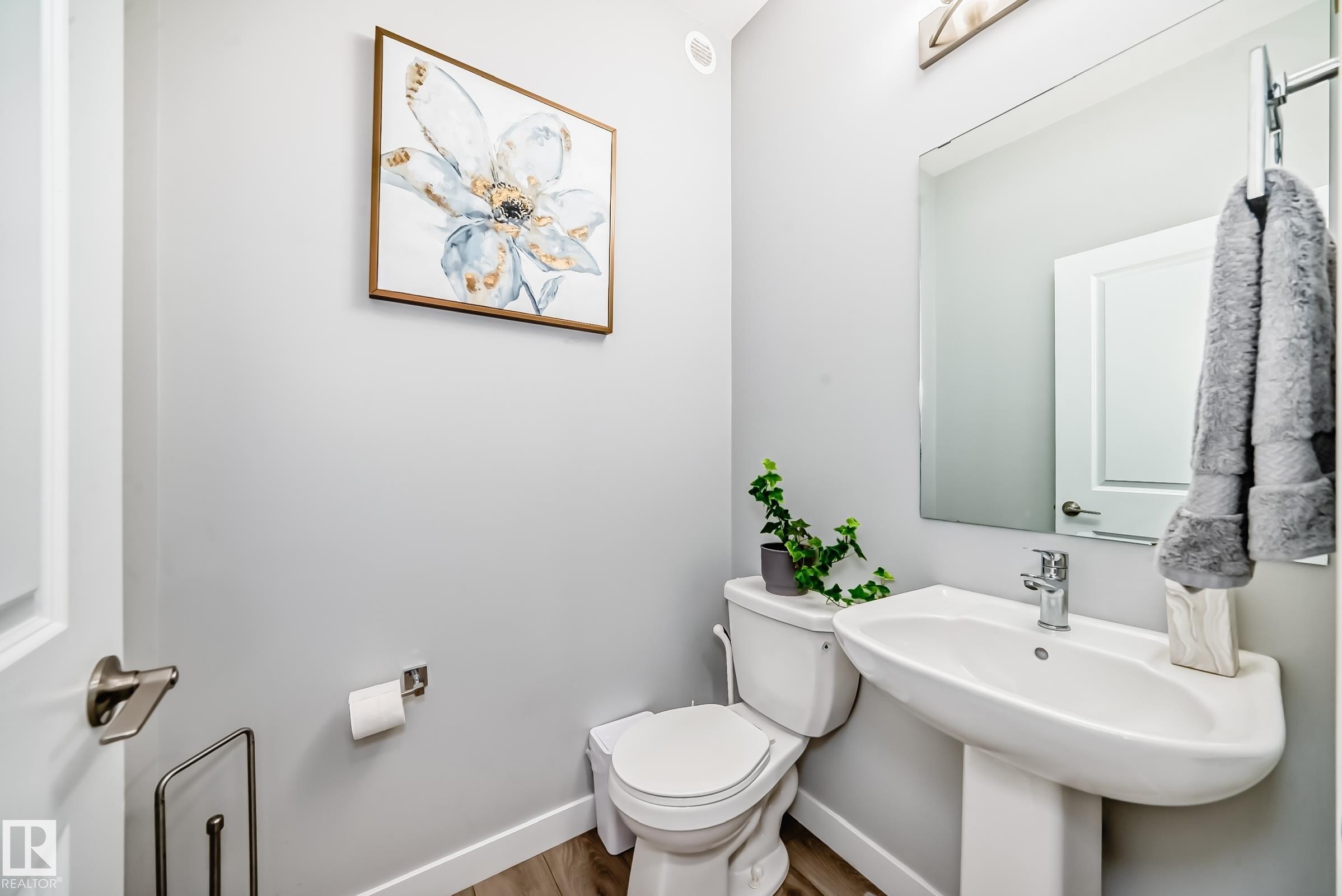Pedestal sink with chrome faucet, large rectangular mirror, and wood-finish flooring - 19635 29 Avenue, Edmonton, AB - Indoor Photo Showing Bathroom