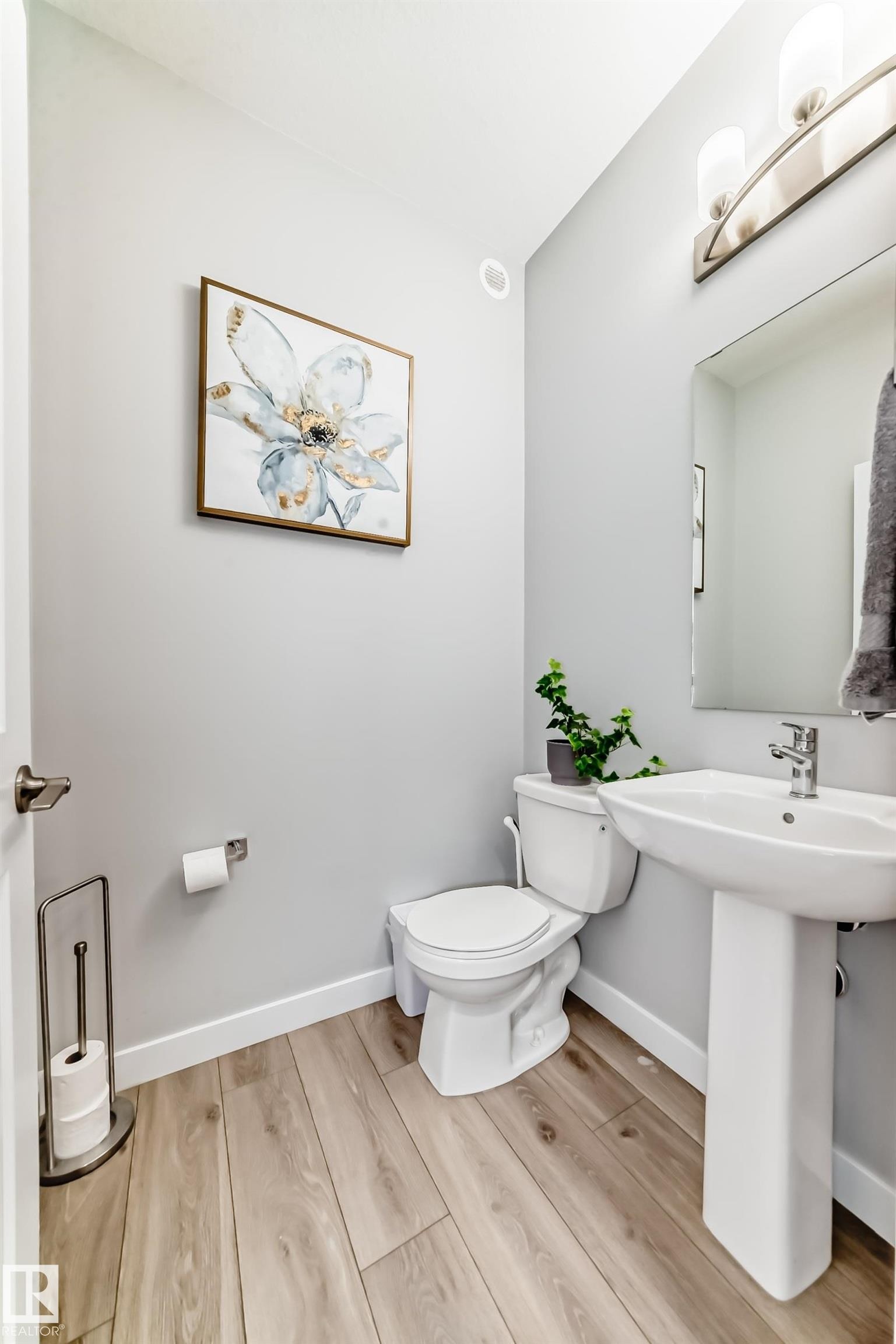 Bathroom featuring a pedestal sink, toilet, wood-finish flooring, and a contemporary vanity light fixture - 19635 29 Avenue, Edmonton, AB - Indoor Photo Showing Bathroom
