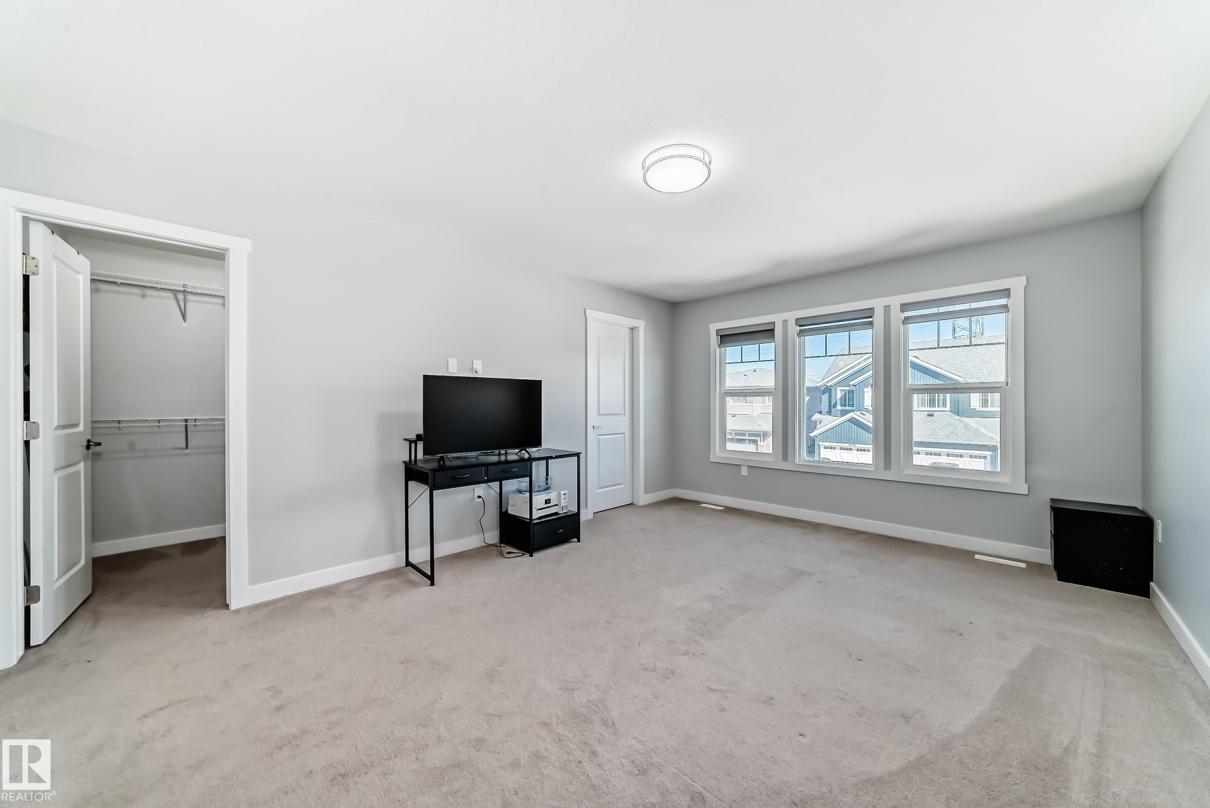 Spacious room featuring light gray walls, plush carpeting, multiple windows providing natural light, a ceiling-mounted light fixture, and an open closet with shelving - 19635 29 Avenue, Edmonton, AB - Indoor
