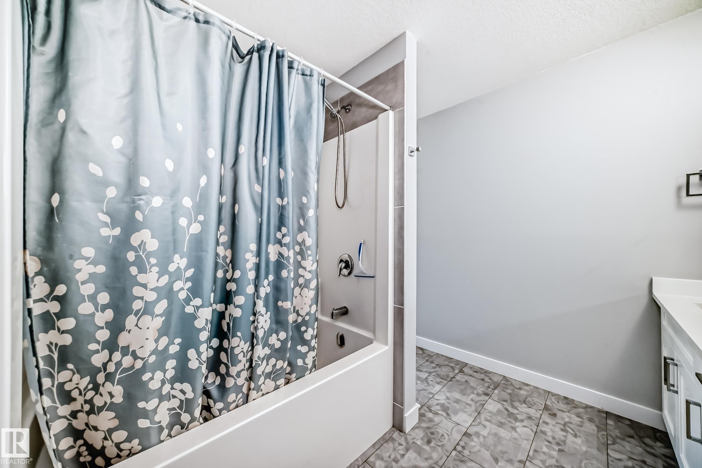 Bathtub with a shower fixture, tile surround, and a coordinating tiled floor - 19635 29 Avenue, Edmonton, AB - Indoor Photo Showing Bathroom