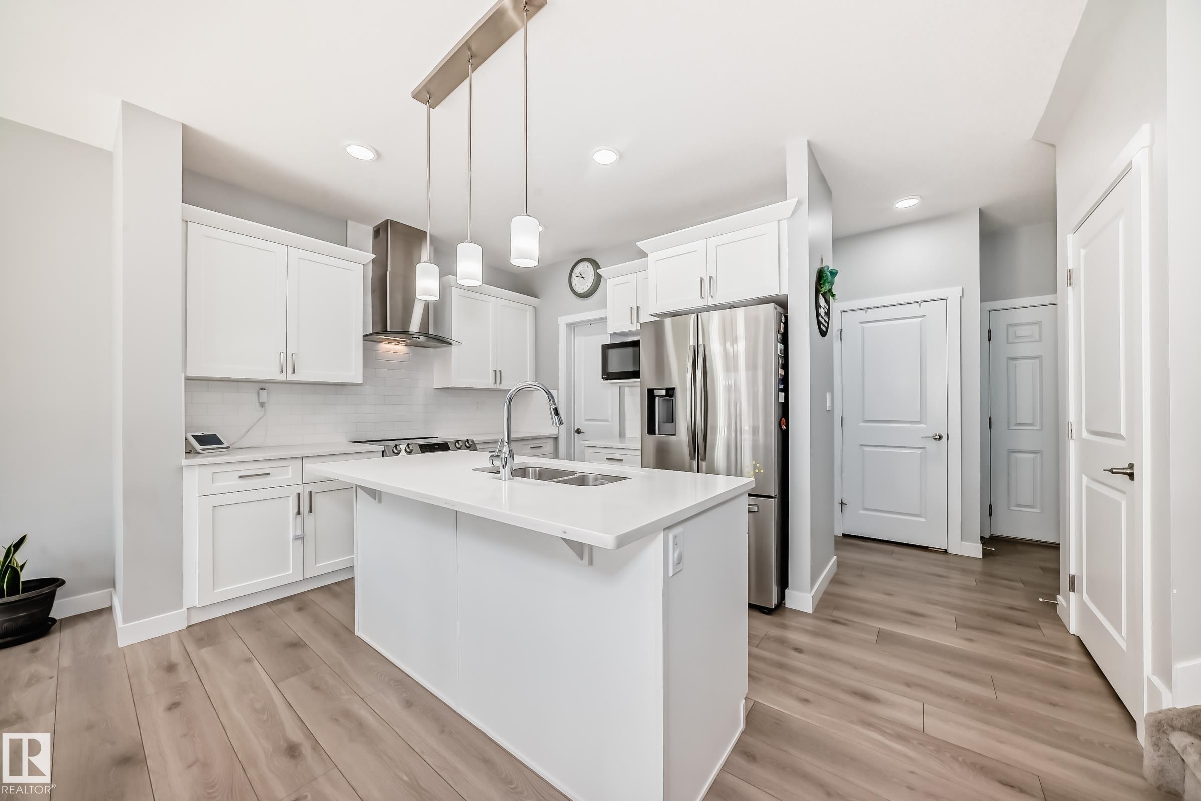 Modern kitchen featuring a central island with an undermount sink, white cabinetry with crown molding, stainless steel appliances, and wood-finish flooring - 19635 29 Avenue, Edmonton, AB - Indoor Photo Showing Kitchen With Double Sink With Upgraded Kitchen