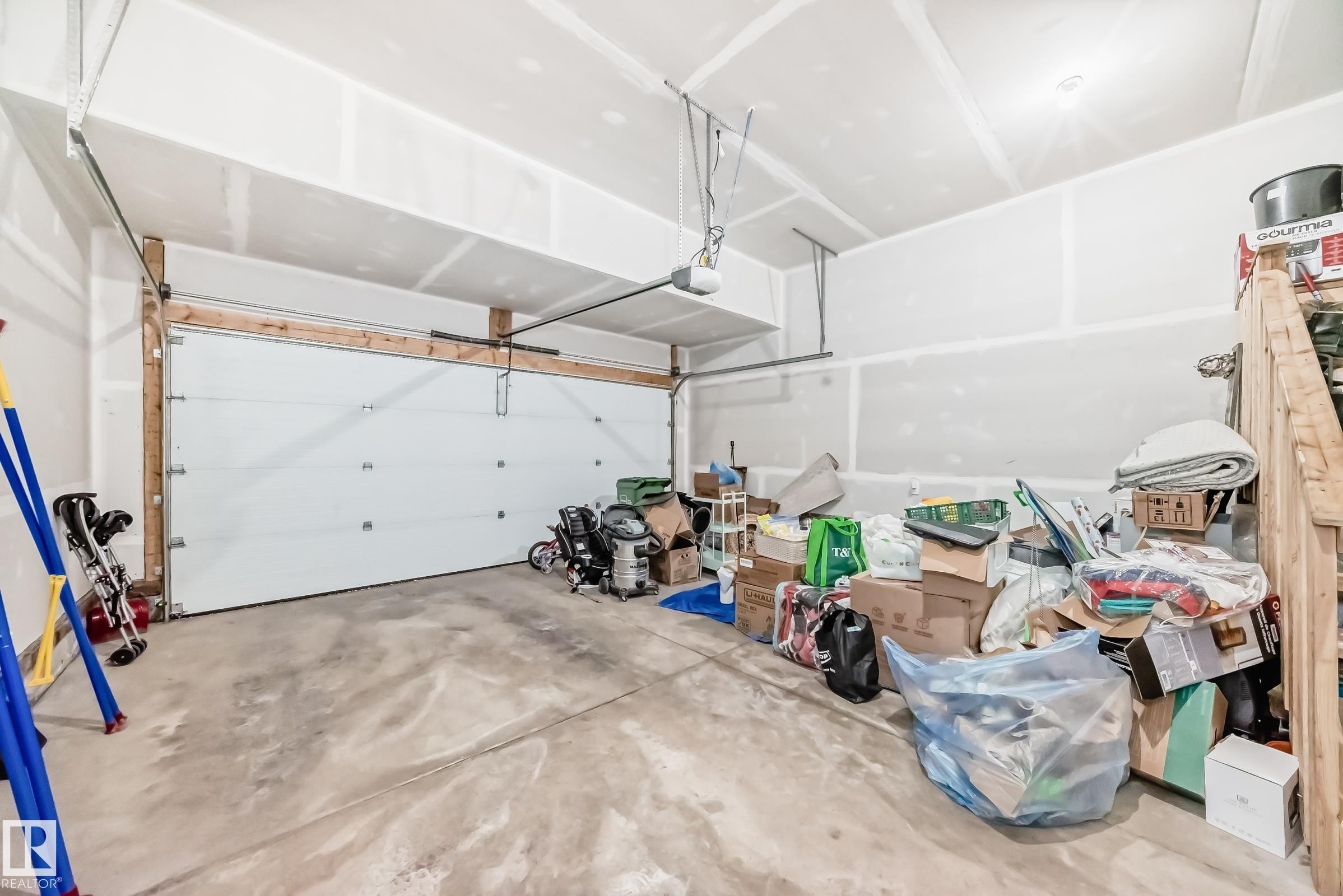 Two-car garage featuring a white sectional overhead door, exposed wood framing, concrete flooring, and an automatic garage door opener - 19635 29 Avenue, Edmonton, AB - Indoor Photo Showing Garage