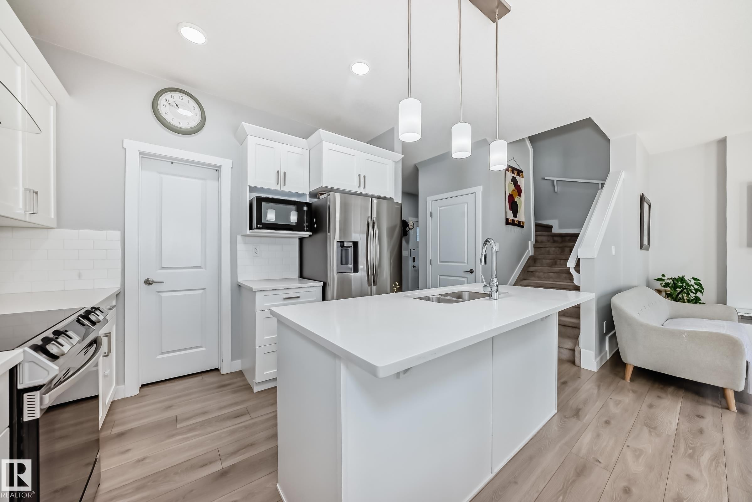 Modern kitchen featuring a large central island with an undermount sink, pendant lighting, stainless steel appliances, white cabinetry, and wood-finish flooring - 19635 29 Avenue, Edmonton, AB - Indoor Photo Showing Kitchen With Double Sink With Upgraded Kitchen