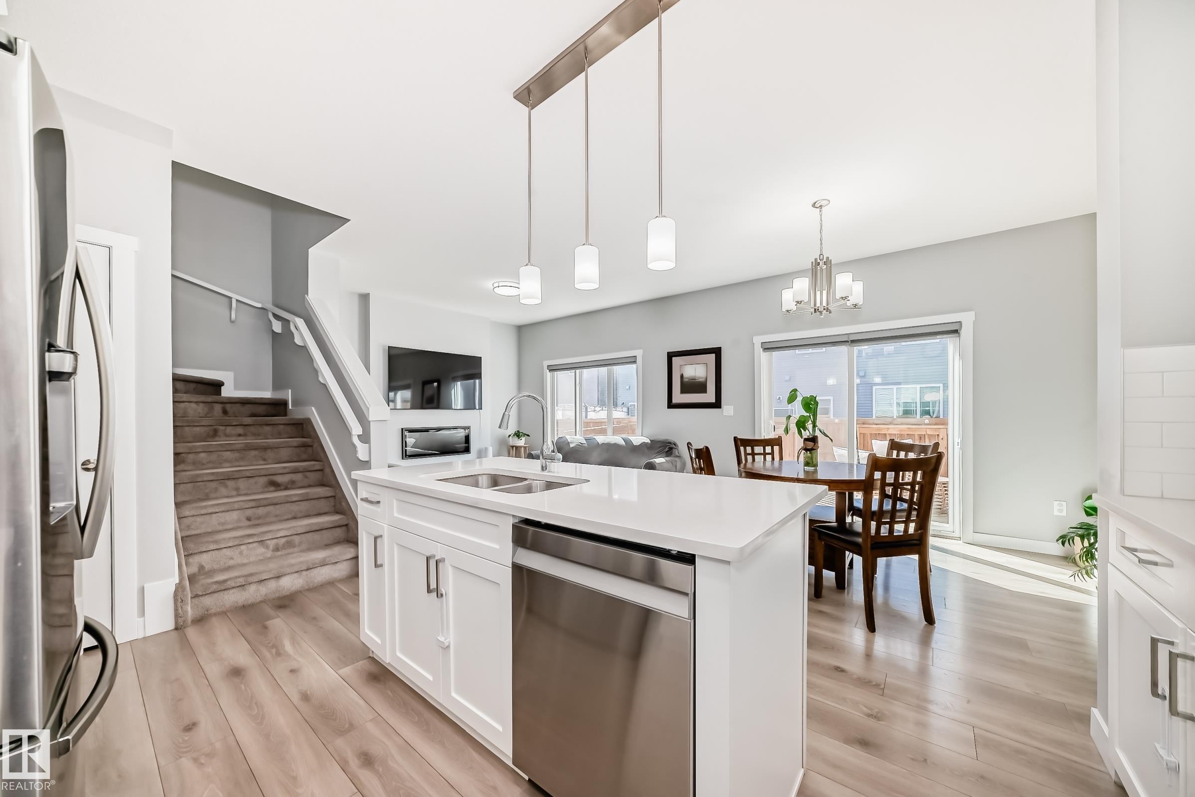 Modern kitchen island featuring a stainless steel dishwasher, double basin sink with a gooseneck faucet, white cabinetry, and a light-toned countertop - 19635 29 Avenue, Edmonton, AB - Indoor Photo Showing Kitchen With Double Sink With Upgraded Kitchen