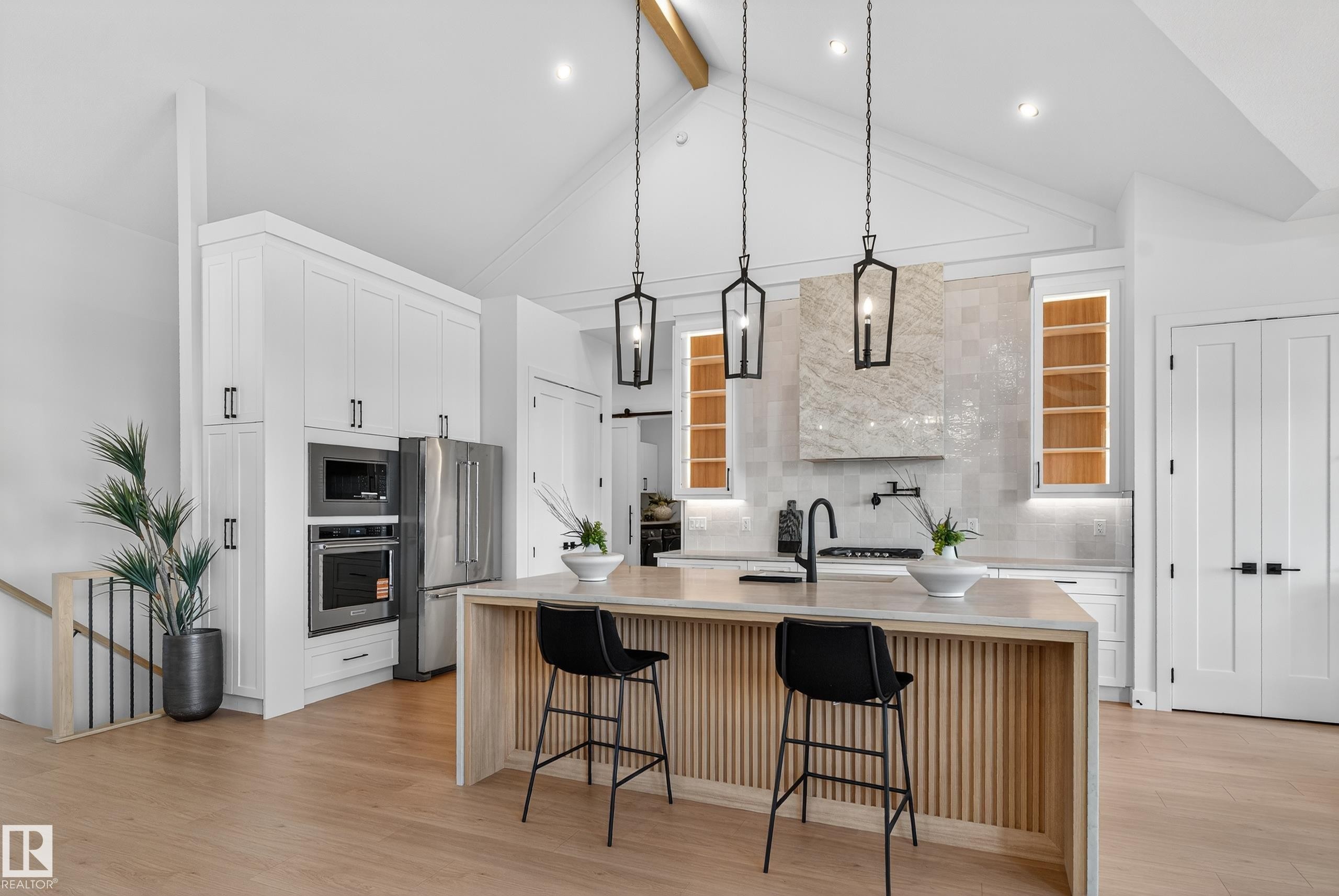 Open-concept kitchen featuring a vaulted ceiling with exposed wood beam, integrated stainless steel appliances, a center island with slat panel detailing, and three pendant light fixtures - 711 166 Avenue, Edmonton, AB - Indoor Photo Showing Kitchen With Upgraded Kitchen