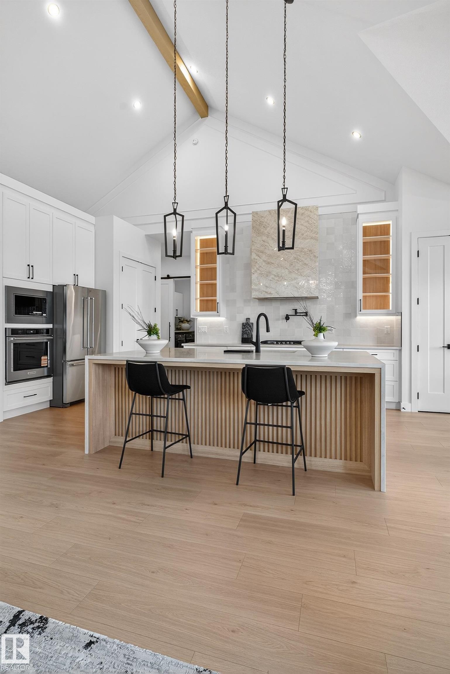 Vaulted ceiling with exposed wood beam, kitchen island with slatted wood paneling, light wood-finish flooring, recessed lighting, and three pendant light fixtures - 711 166 Avenue, Edmonton, AB - Indoor Photo Showing Kitchen With Upgraded Kitchen
