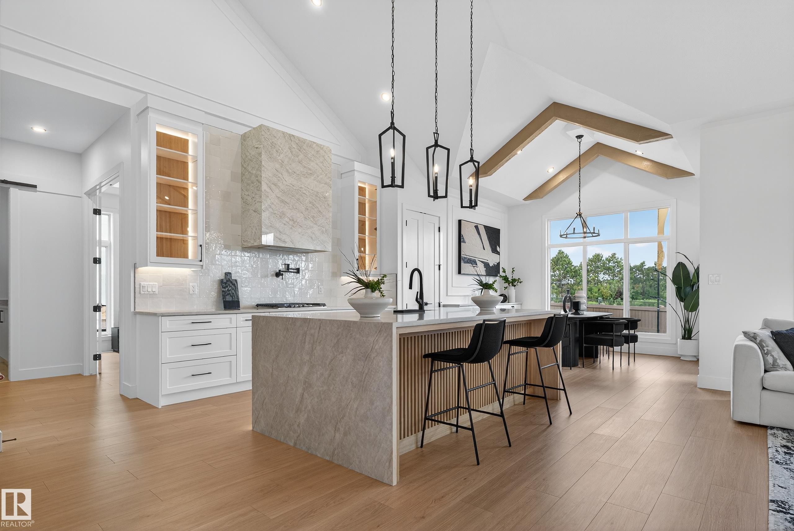 Gourmet kitchen featuring a large central island, light wood-finish flooring, white cabinetry, a custom range hood, and vaulted ceilings with exposed beams - 711 166 Avenue, Edmonton, AB - Indoor Photo Showing Kitchen With Upgraded Kitchen