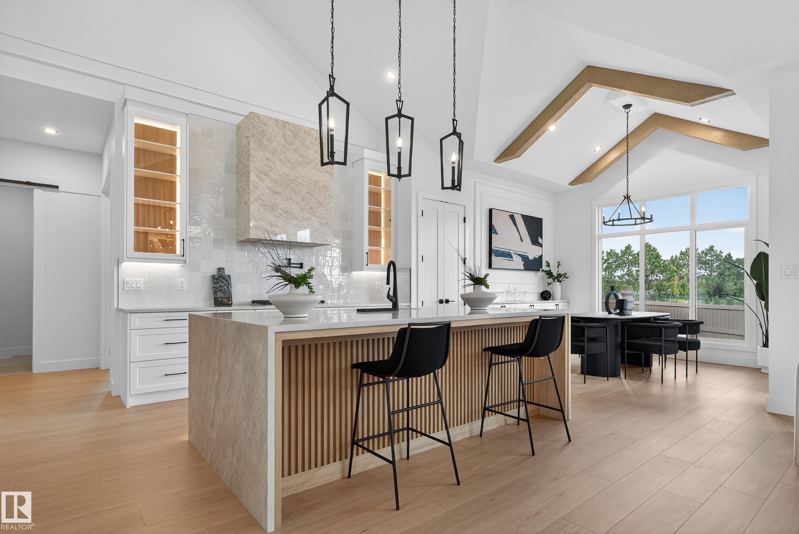 Modern kitchen featuring a large central island with slatted wood detailing, white cabinetry, a stone-clad range hood, and light wood-finish flooring - 711 166 Avenue, Edmonton, AB - Indoor