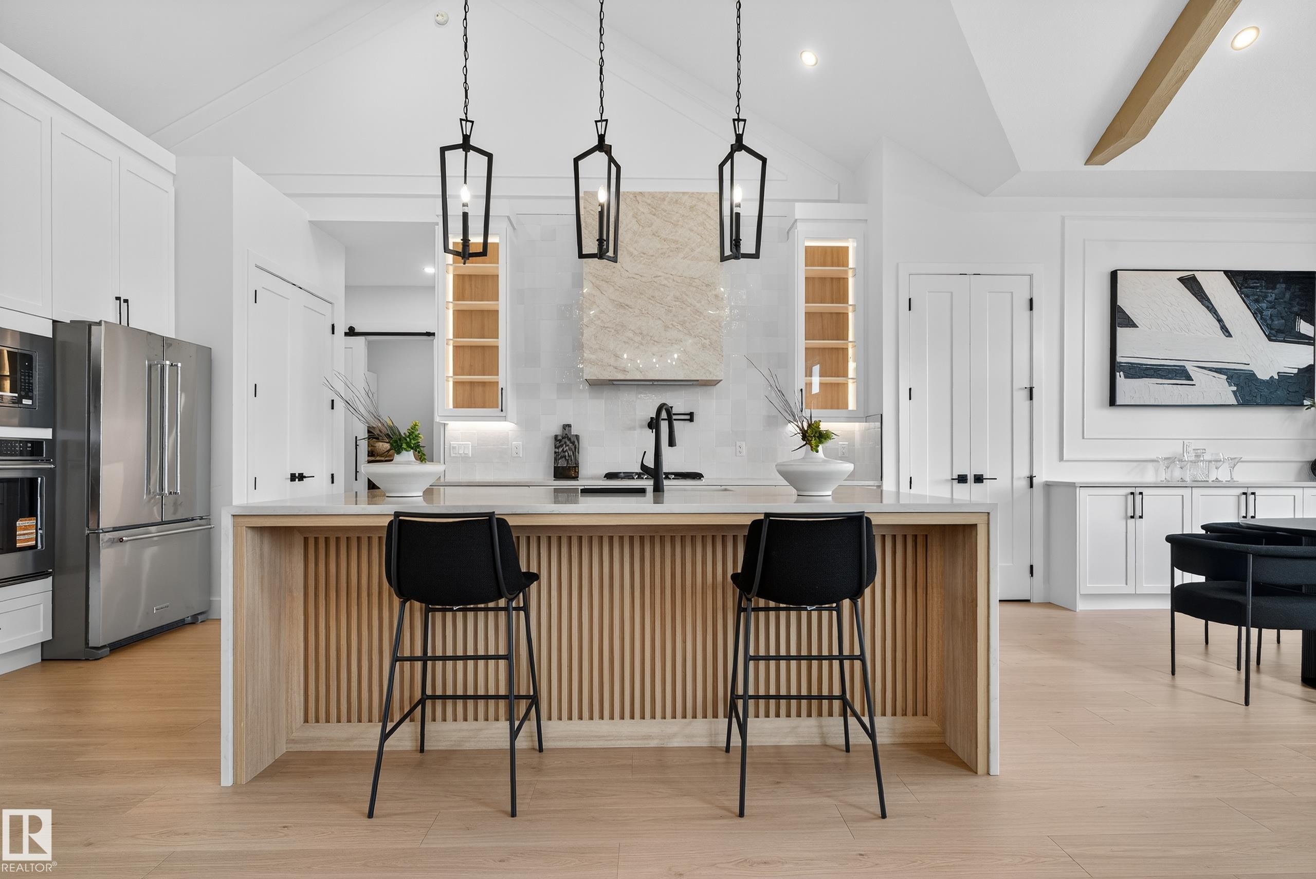 Contemporary kitchen featuring a light wood-finish island with vertical slat detailing, a light countertop, and three black pendant lights - 711 166 Avenue, Edmonton, AB - Indoor Photo Showing Kitchen With Upgraded Kitchen