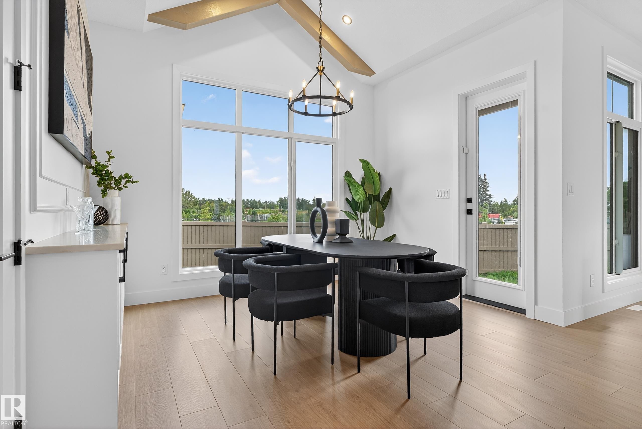 Dining area featuring extensive natural light from large windows, light wood-finish flooring, a built-in buffet with light countertop, a vaulted ceiling with exposed beam, and a black wrought iron chandelier - 711 166 Avenue, Edmonton, AB - Indoor Photo Showing Dining Room