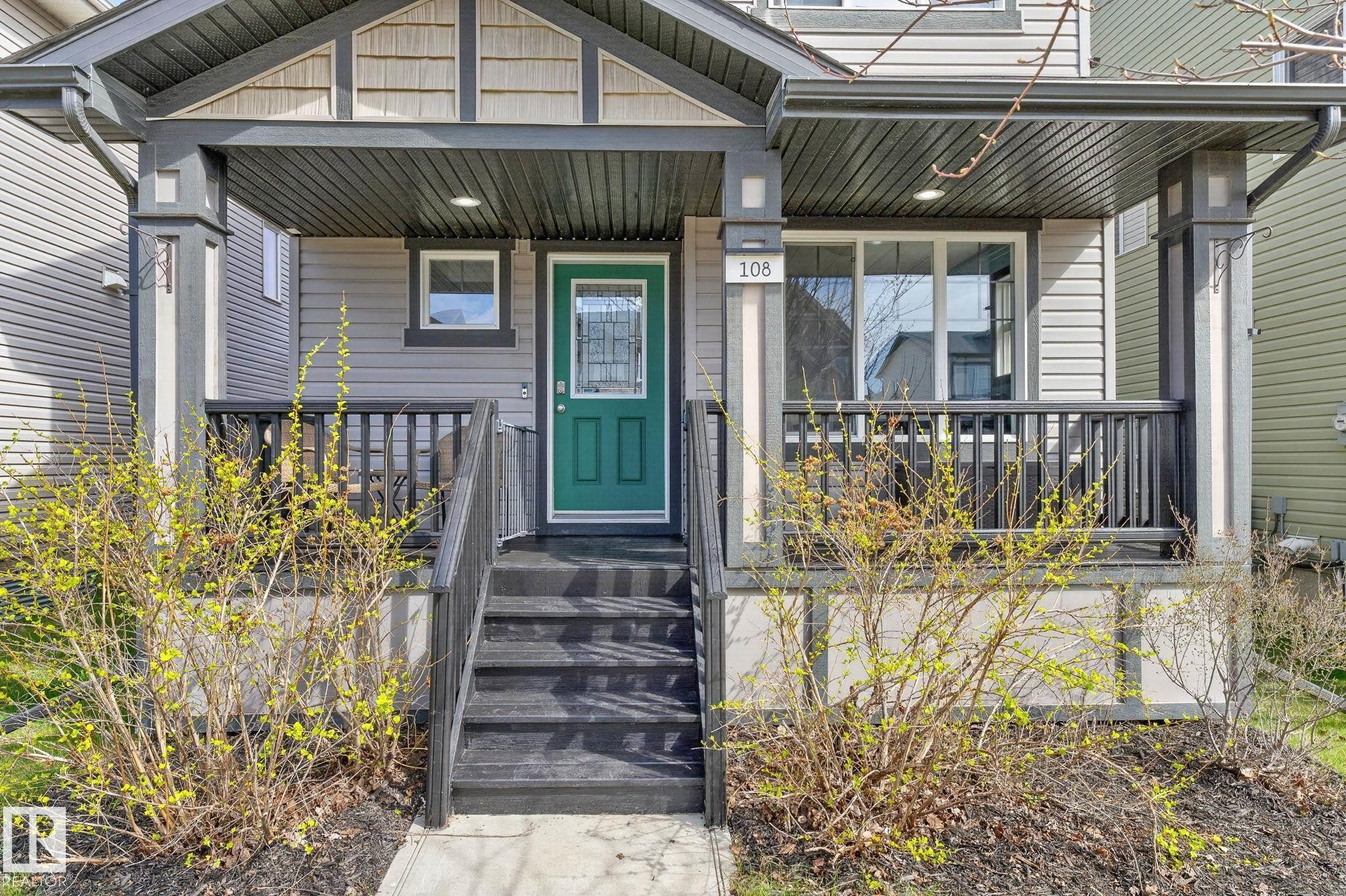 Inviting covered front porch with dark railings and steps, complemented by a vibrant green entry door with decorative glass - 108 Hewitt Circle, Spruce Grove, AB - Outdoor