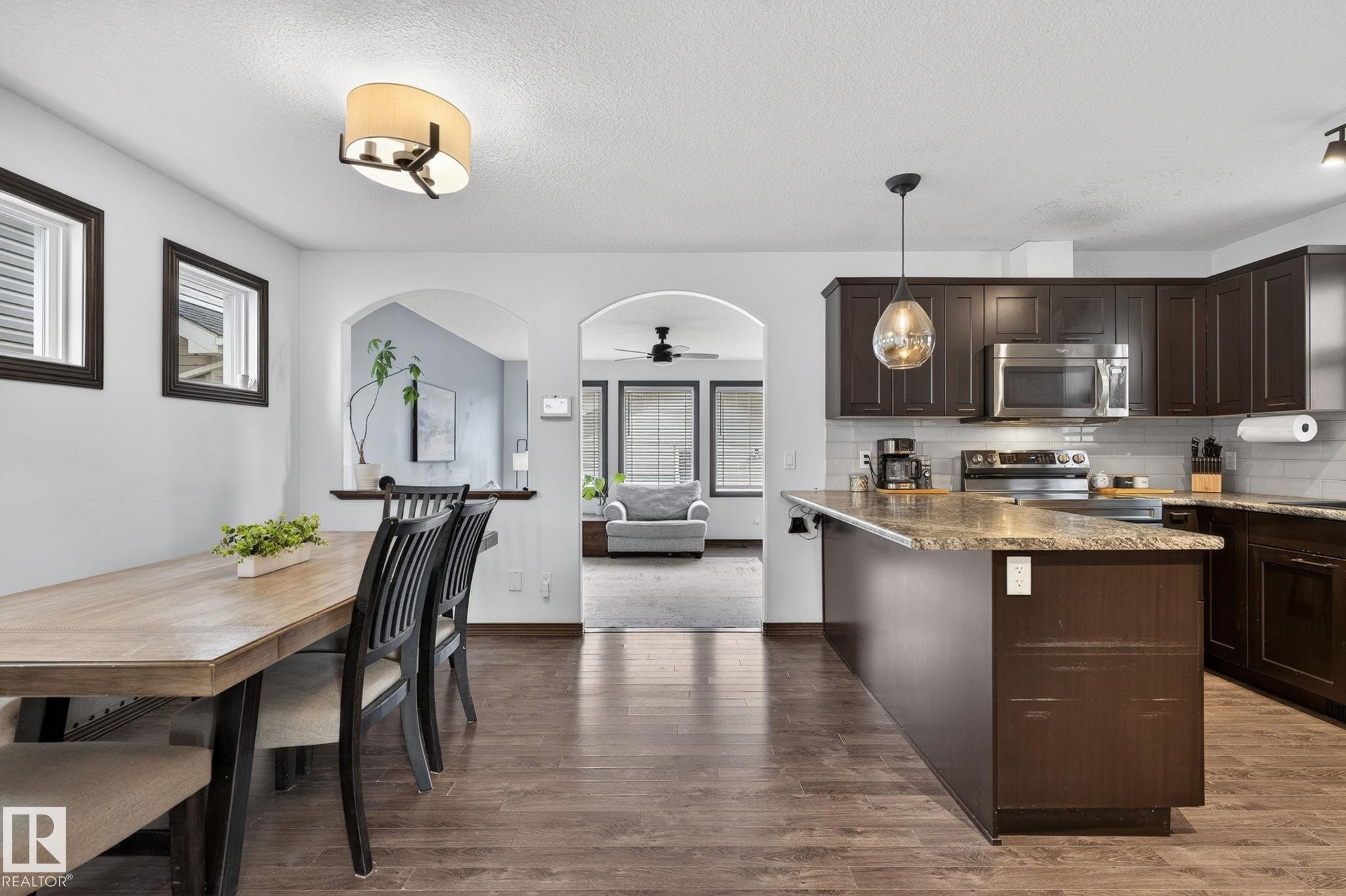 Kitchen featuring dark wood-finish cabinetry, stainless steel appliances, a white subway tile backsplash, and a peninsula with a stone-finish countertop - 108 Hewitt Circle, Spruce Grove, AB - Indoor