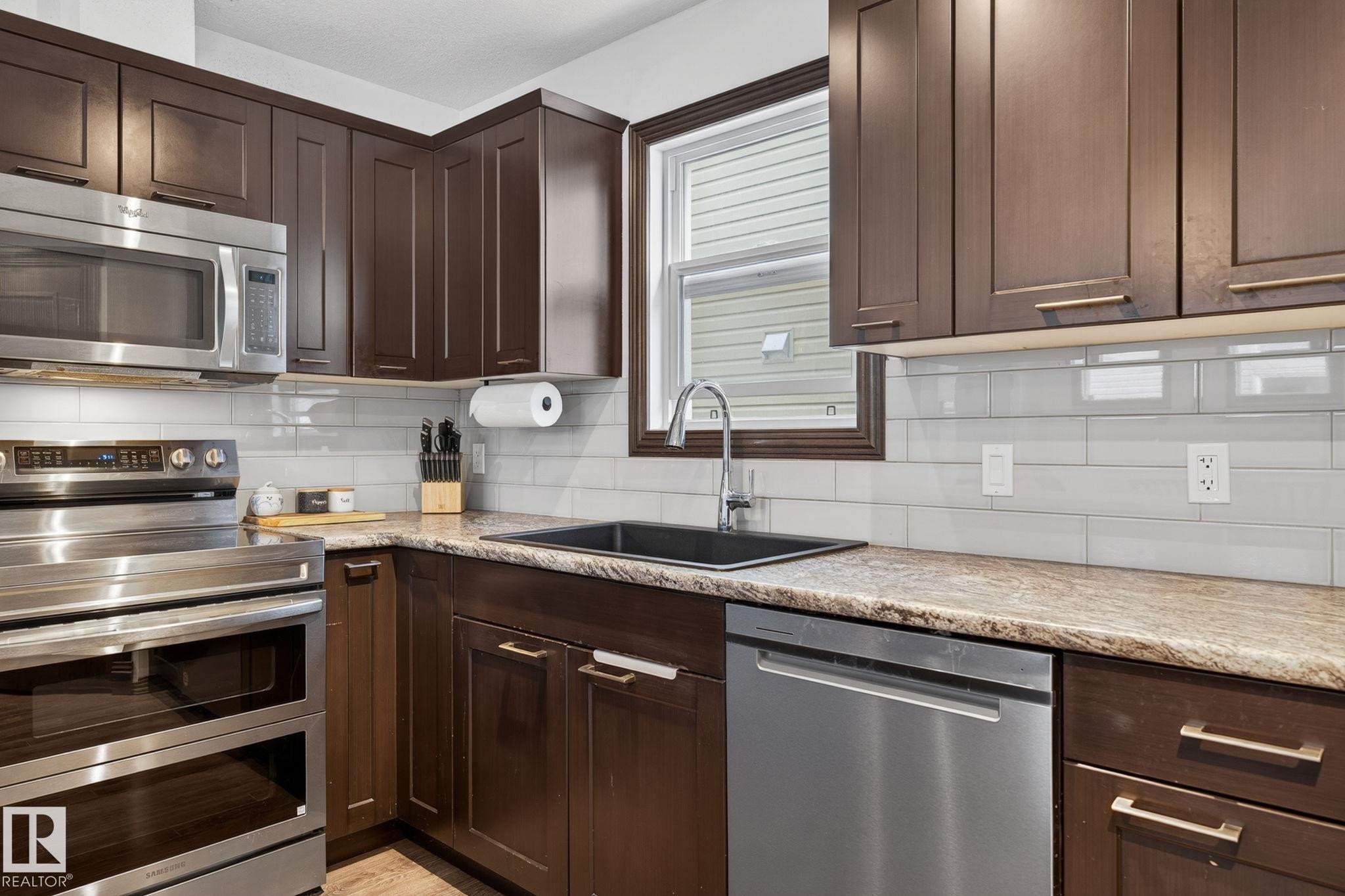 Kitchen featuring dark wood-finish cabinetry, stainless steel appliances, a black undermount sink, and light-toned countertops - 108 Hewitt Circle, Spruce Grove, AB - Indoor Photo Showing Kitchen With Upgraded Kitchen