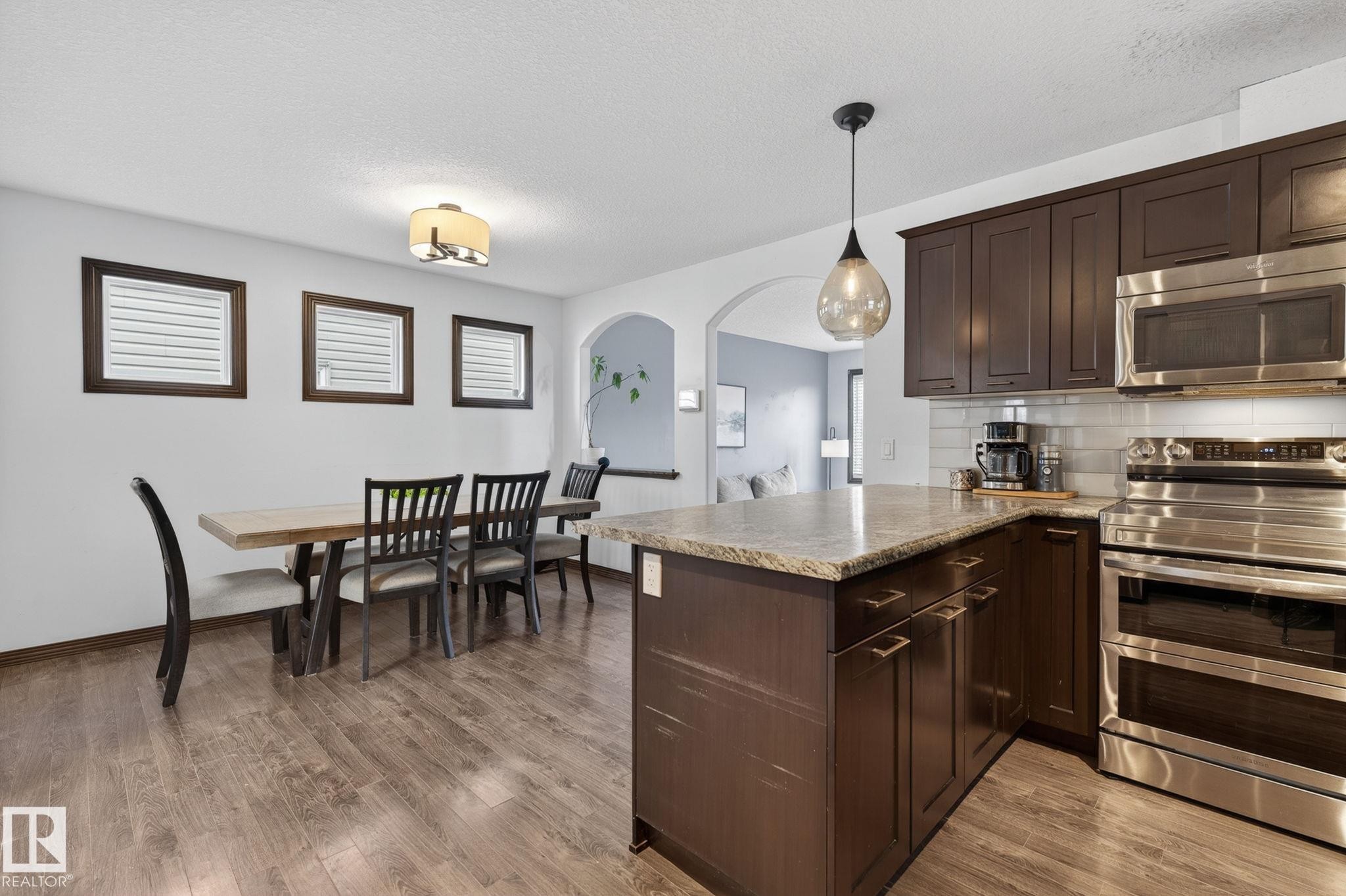 Kitchen featuring dark wood-finish cabinetry, stainless steel appliances, a light-toned countertop, and a subway tile backsplash - 108 Hewitt Circle, Spruce Grove, AB - Indoor