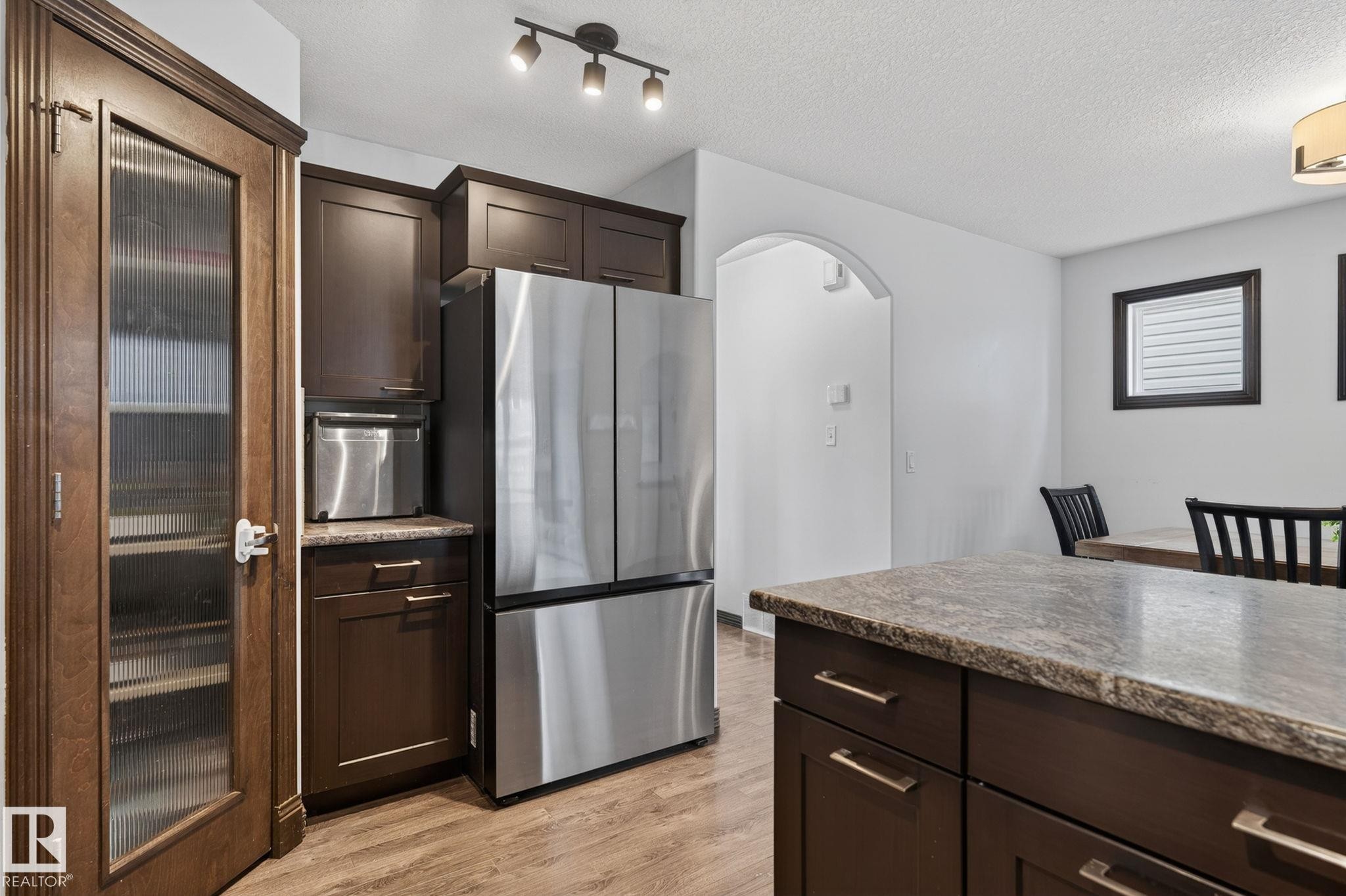 Kitchen featuring wood-finish flooring, dark wood cabinetry, and a stainless steel refrigerator - 108 Hewitt Circle, Spruce Grove, AB - Indoor Photo Showing Kitchen
