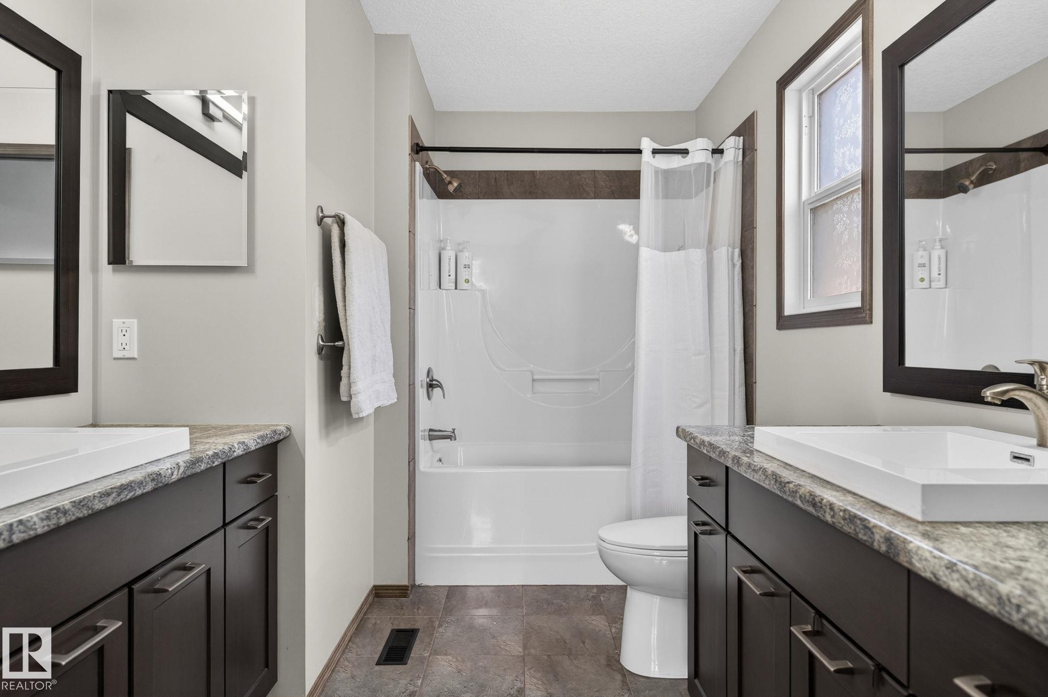 Bathroom featuring dual dark wood vanities with light stone-look countertops, rectangular undermount sinks, and brushed nickel fixtures - 108 Hewitt Circle, Spruce Grove, AB - Indoor Photo Showing Bathroom