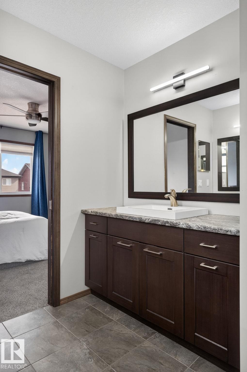 Bathroom vanity featuring dark wood cabinetry, a light-toned countertop, and an integrated rectangular sink with a gold-finish faucet - 108 Hewitt Circle, Spruce Grove, AB - Indoor