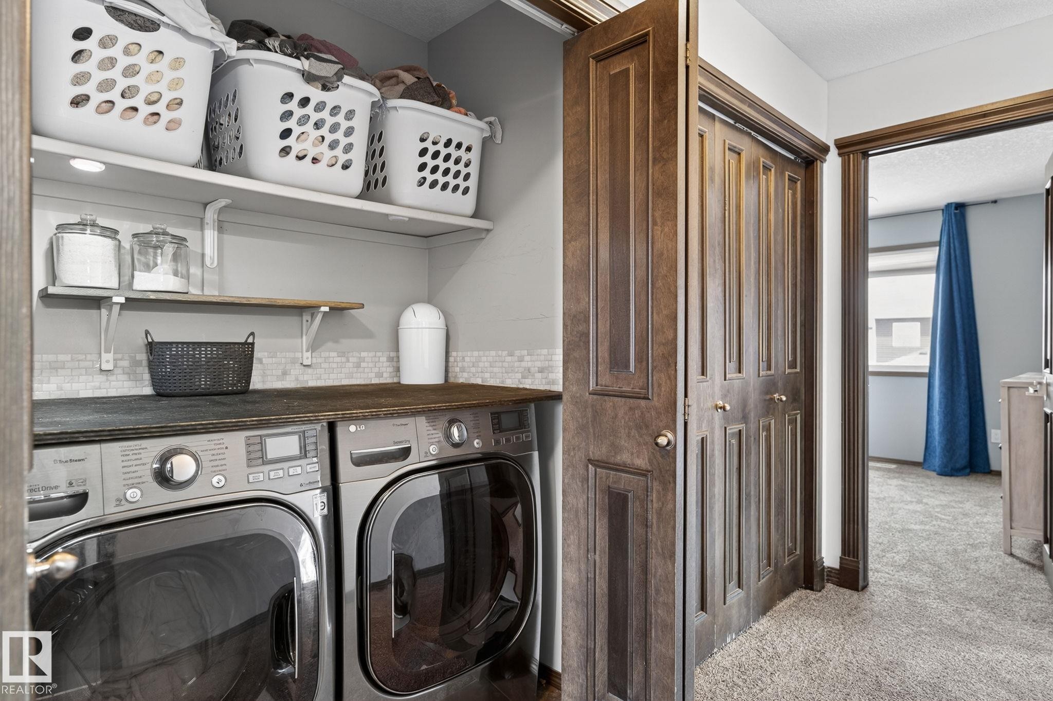 Dedicated laundry area featuring a wood-finish countertop, subway tile backsplash, and two wall-mounted shelves - 108 Hewitt Circle, Spruce Grove, AB - Indoor Photo Showing Laundry Room