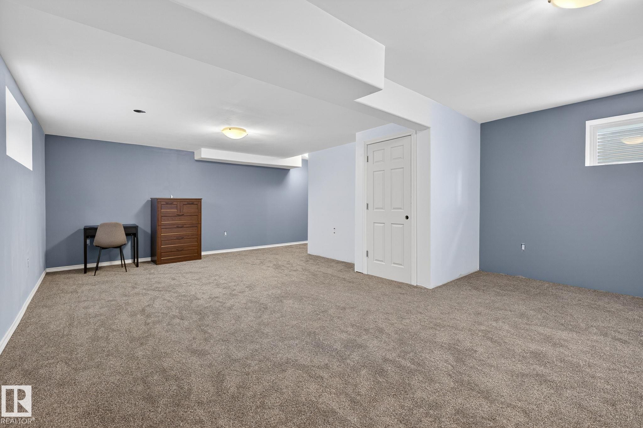 Spacious room featuring neutral carpet flooring, blue-painted walls, white trim, and a white paneled door - 108 Hewitt Circle, Spruce Grove, AB - Indoor