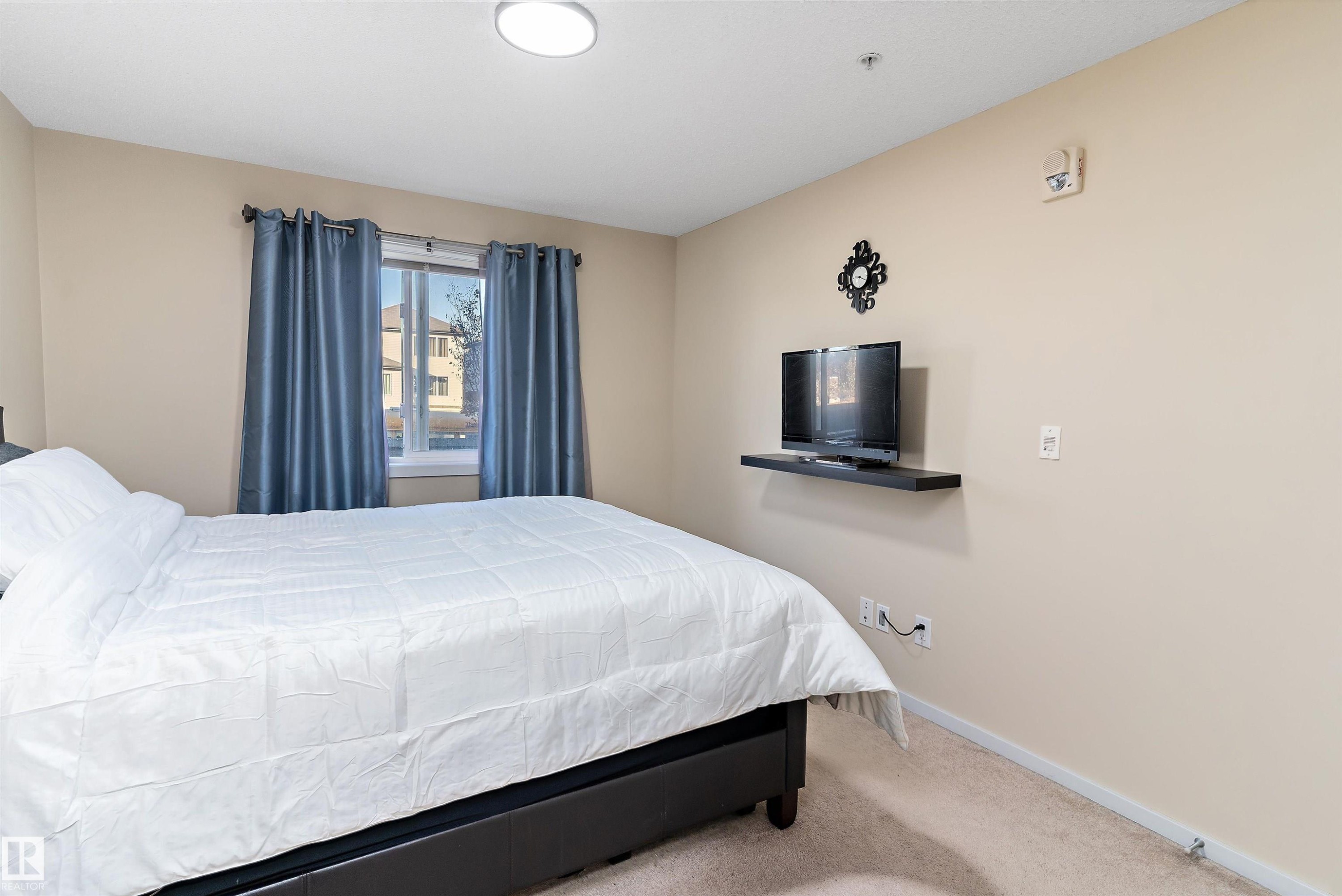Bedroom featuring a window with blue drapes, neutral wall paint, overhead flush-mount lighting, and carpet flooring - 122 3357 16A Avenue, Edmonton, AB - Indoor Photo Showing Bedroom