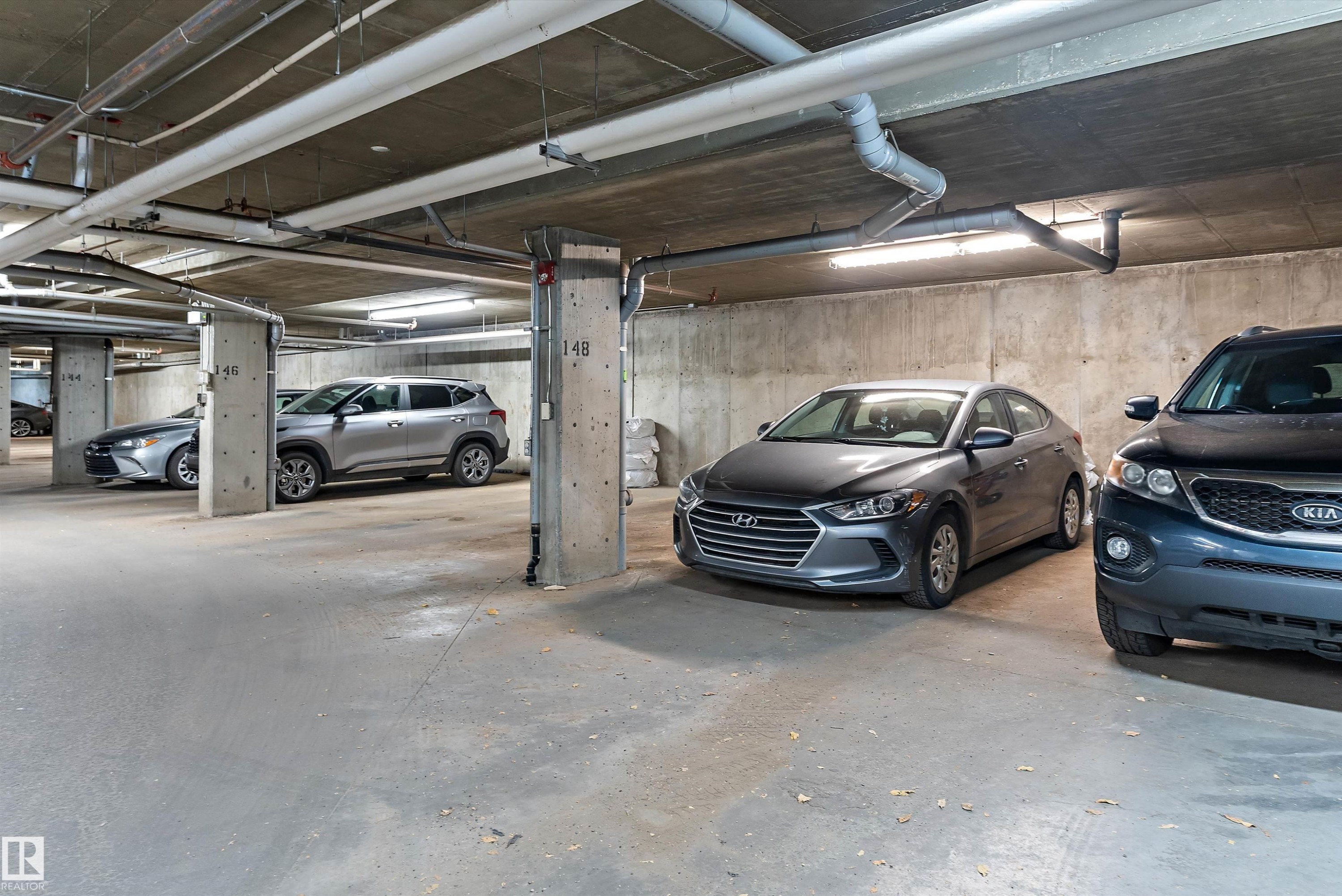 Underground parking garage featuring concrete flooring, concrete walls, concrete support columns, exposed overhead utilities, and fluorescent lighting - 122 3357 16A Avenue, Edmonton, AB - Indoor Photo Showing Garage
