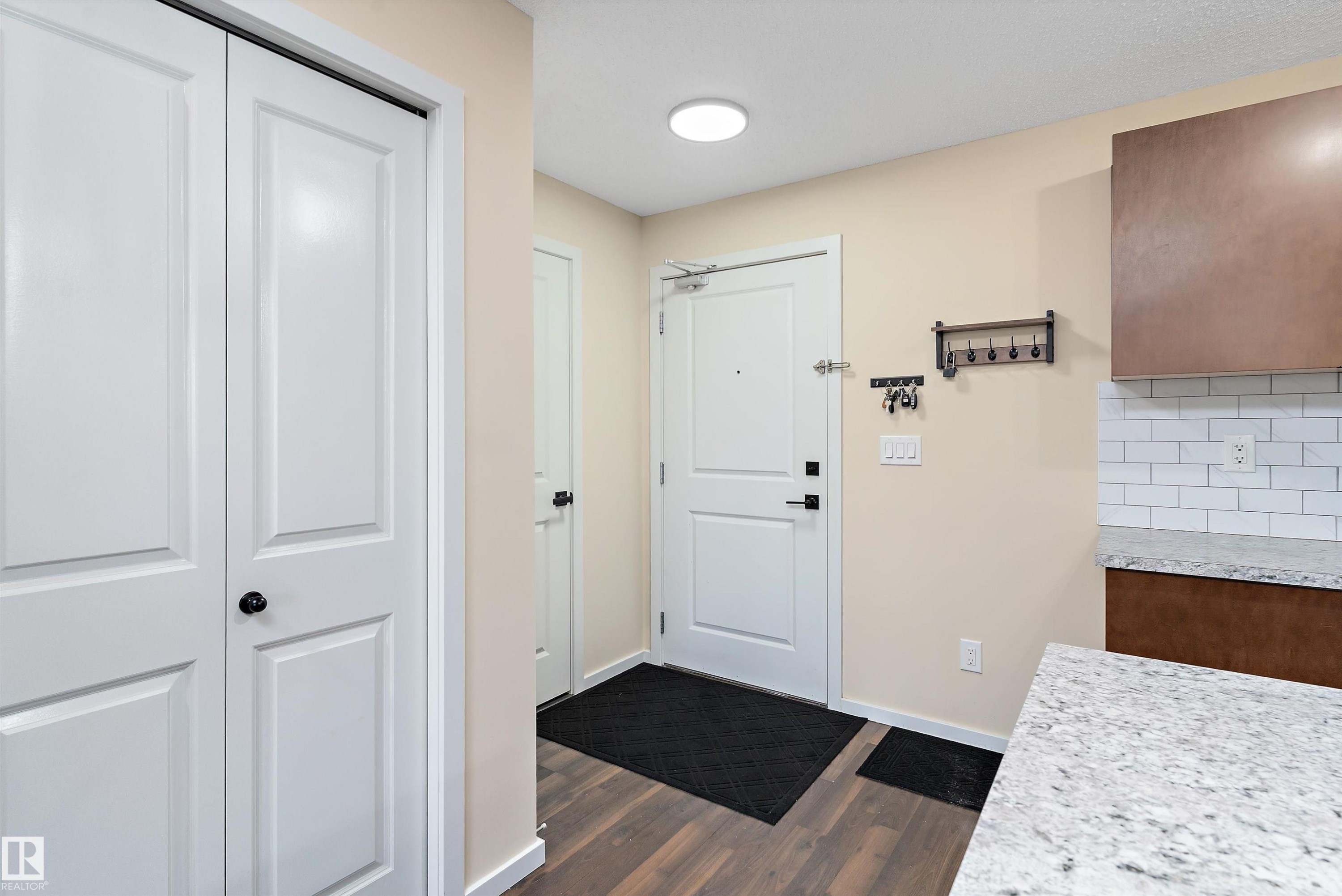 Entryway featuring wood-finish flooring, a white paneled door, and a built-in closet with bifold doors - 122 3357 16A Avenue, Edmonton, AB - Indoor