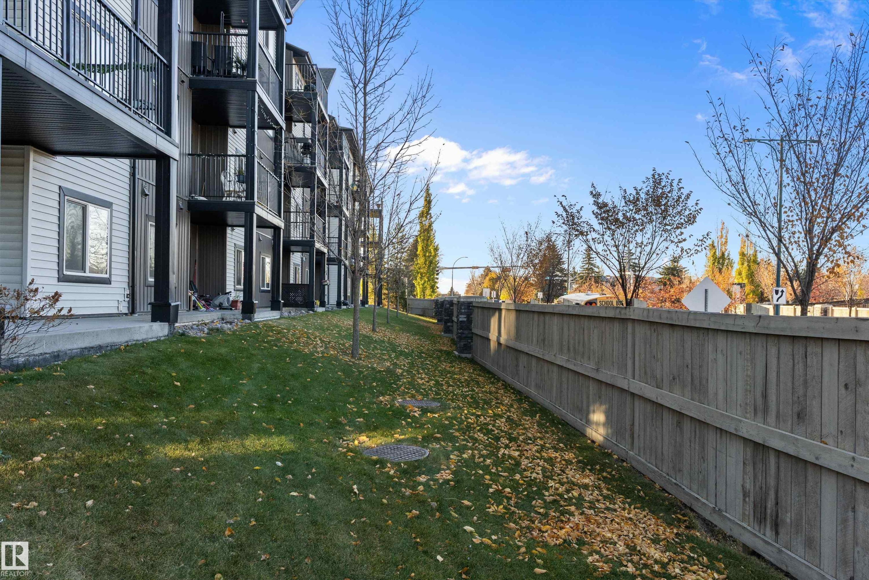 Multi-story residential building featuring balconies with black railings, horizontal siding, and a sloped grassy area - 122 3357 16A Avenue, Edmonton, AB - Outdoor