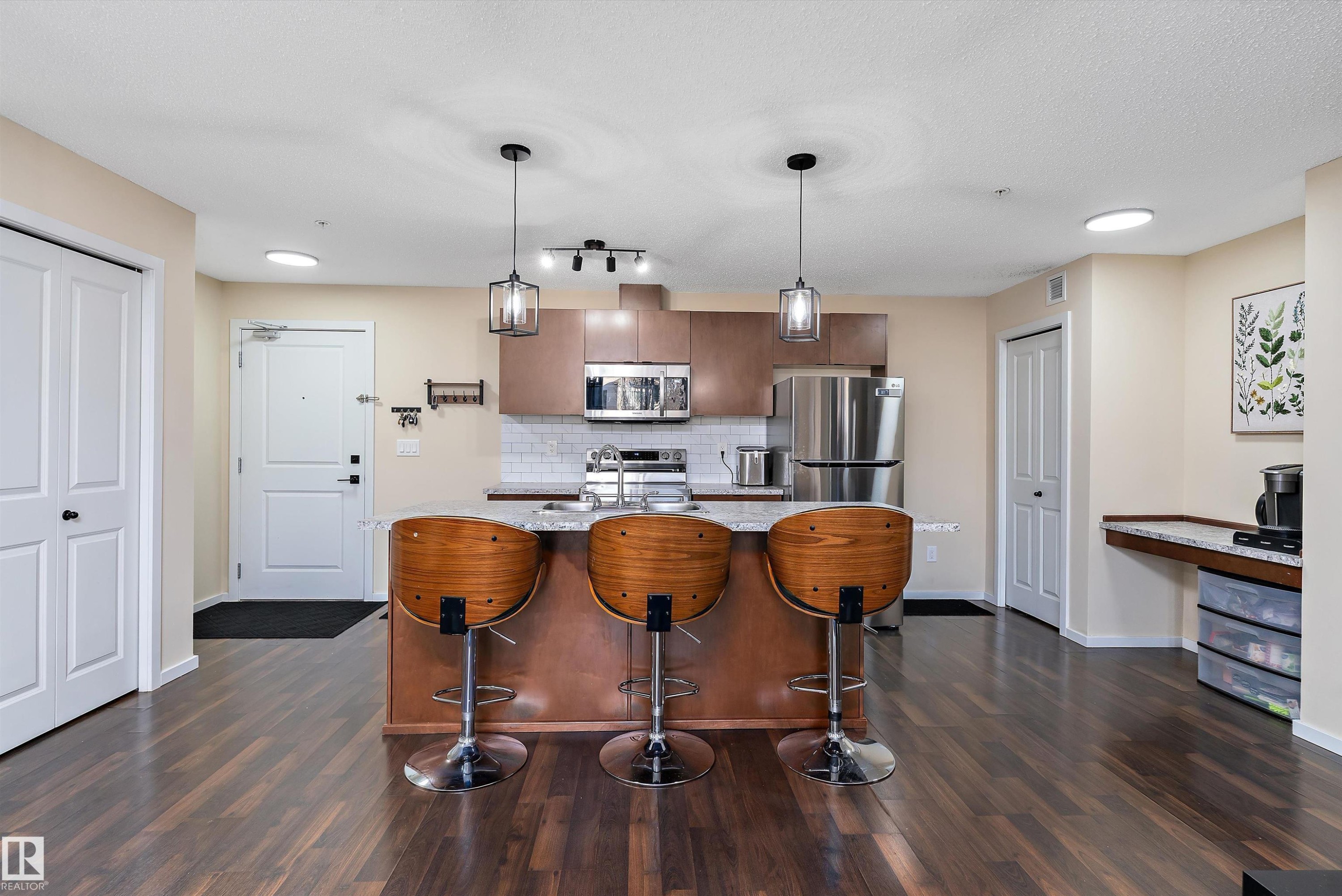 Open-concept kitchen featuring wood-finish flooring, a central island with a granite-style countertop, stainless steel appliances, and pendant lighting - 122 3357 16A Avenue, Edmonton, AB - Indoor Photo Showing Kitchen With Upgraded Kitchen
