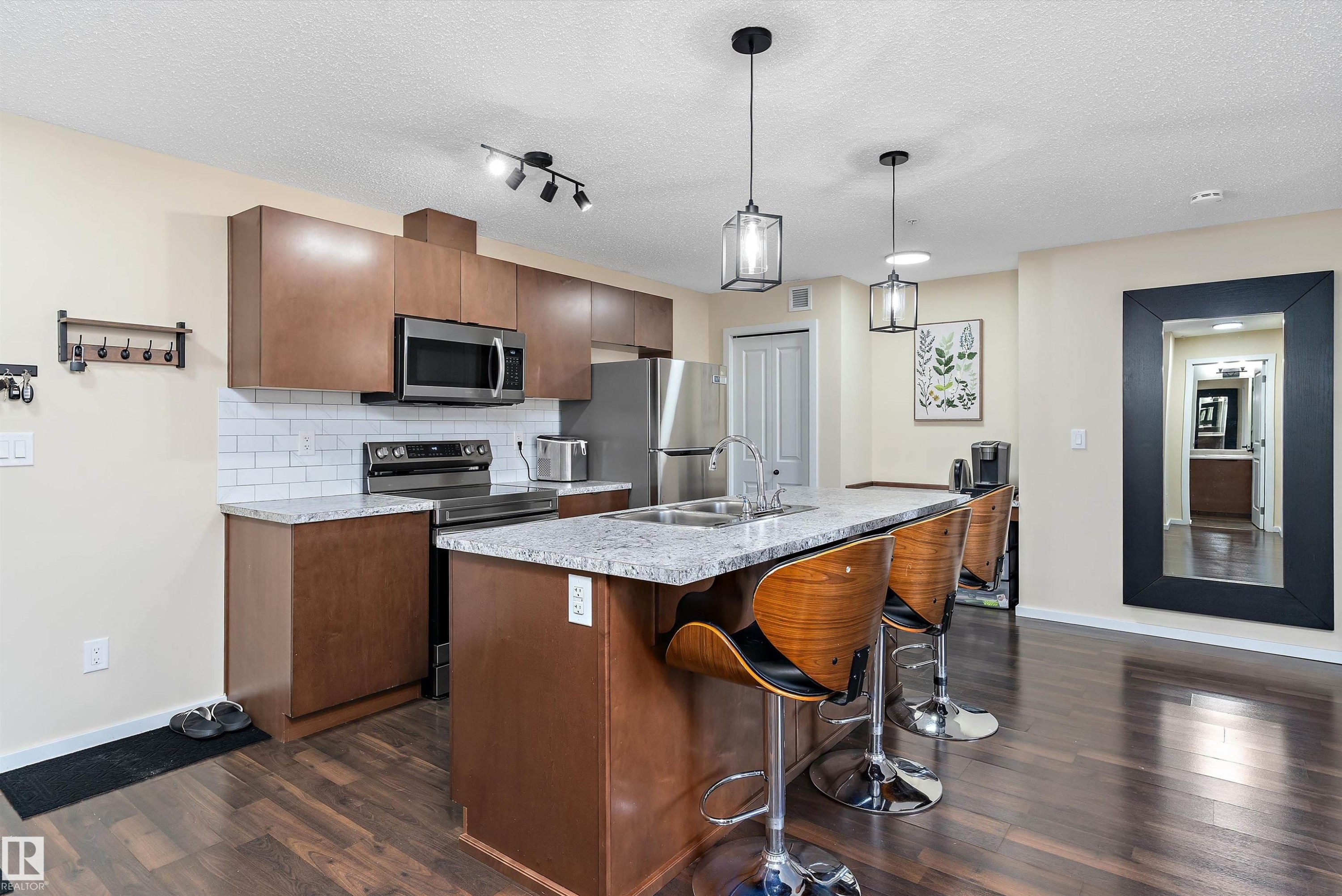 Open-concept kitchen featuring wood-finish flooring, stainless steel appliances, a white subway tile backsplash, light-toned countertops, and a kitchen island with pendant lighting - 122 3357 16A Avenue, Edmonton, AB - Indoor Photo Showing Kitchen With Double Sink With Upgraded Kitchen