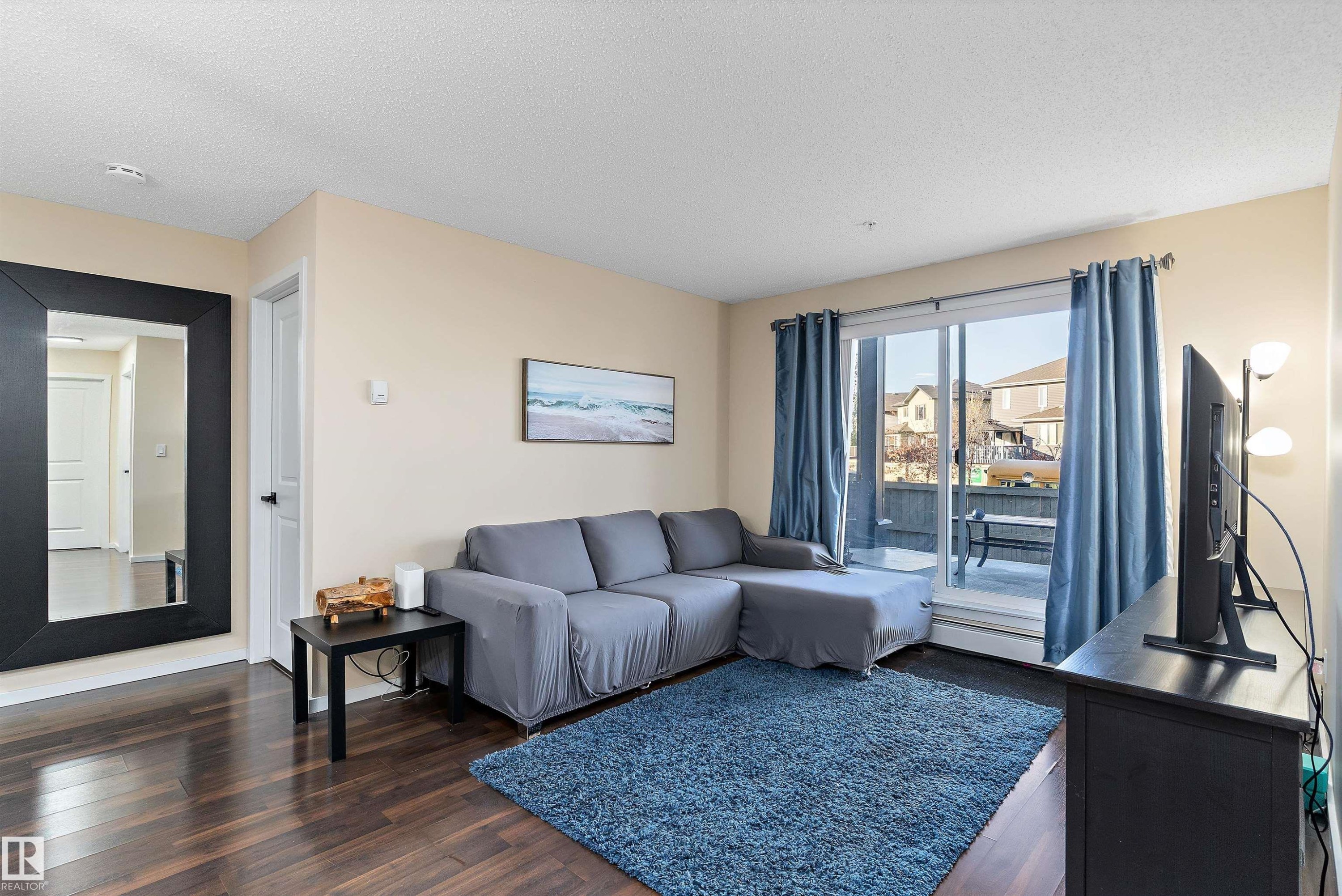 Living area featuring dark wood-finish flooring, light neutral wall paint, and a sliding glass door leading to an outdoor patio - 122 3357 16A Avenue, Edmonton, AB - Indoor Photo Showing Living Room
