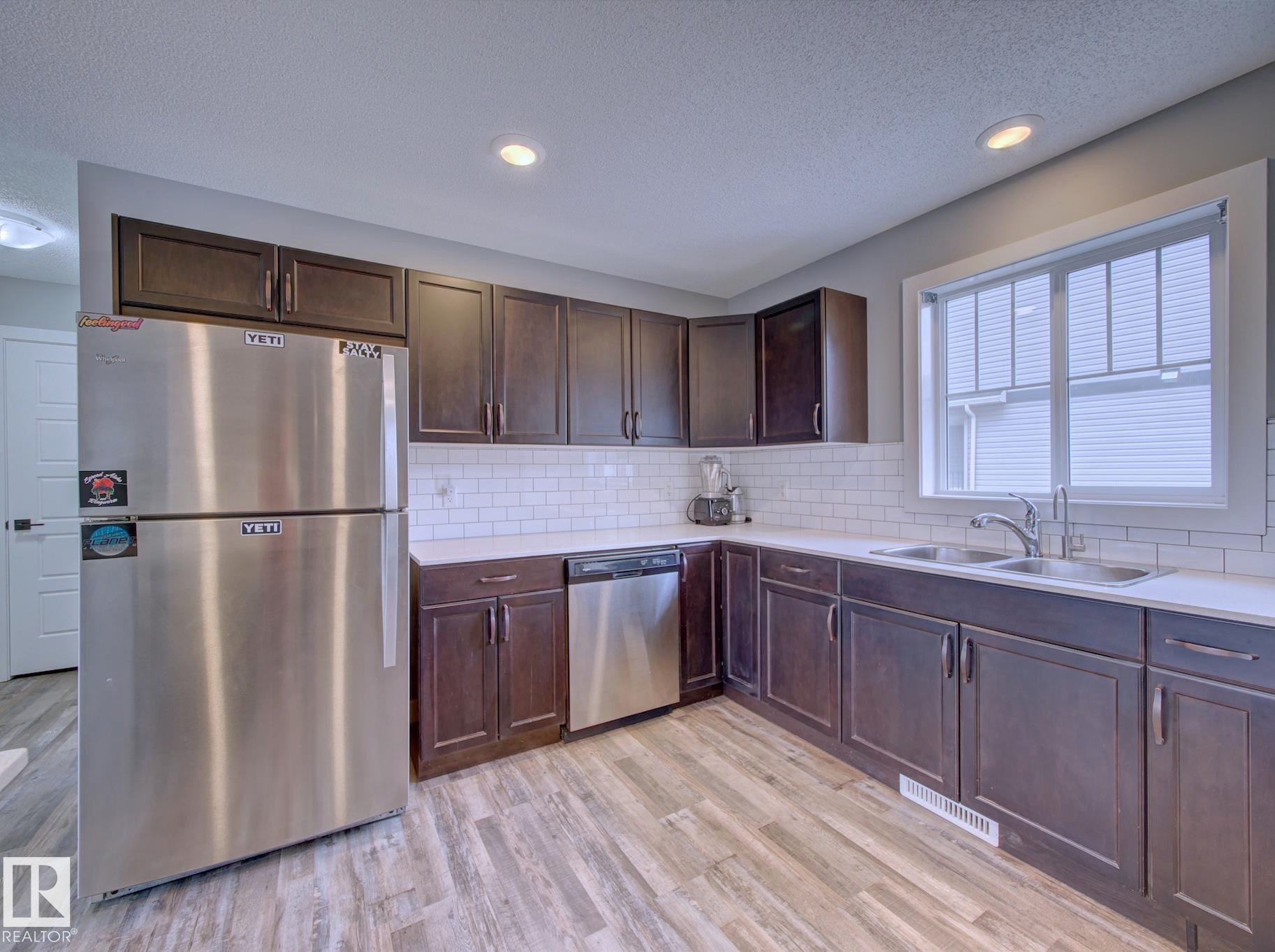 Kitchen featuring dark wood cabinetry, white subway tile backsplash, light countertops, and wood-finish flooring - 11 165 Cy Becker Boulevard, Edmonton, AB - Indoor Photo Showing Kitchen With Stainless Steel Kitchen