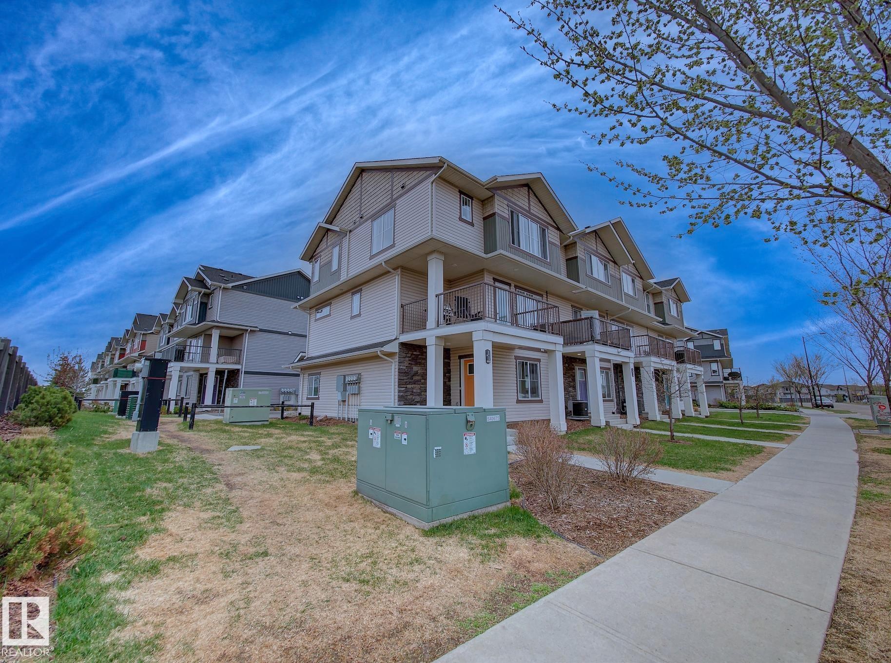 Modern multi-story residential building featuring light-toned siding, stone accents, multiple balconies with glass railings, and prominent dormer windows - 11 165 Cy Becker Boulevard, Edmonton, AB - Outdoor With Facade