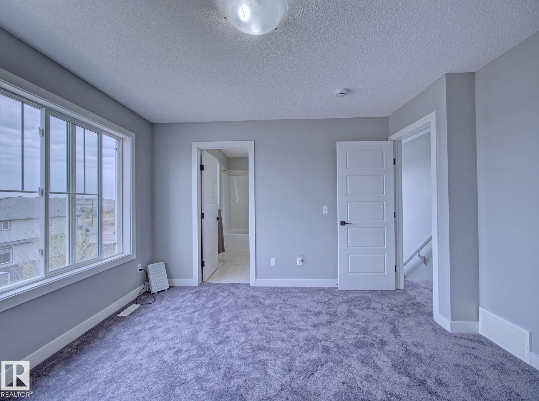 Spacious room featuring plush gray carpeting, a large multipane window, and contemporary white trim - 11 165 Cy Becker Boulevard, Edmonton, AB - Indoor Photo Showing Other Room
