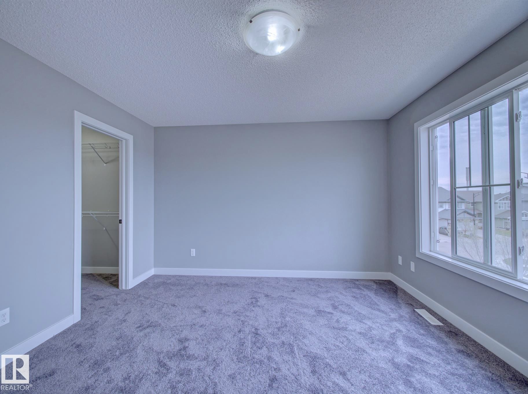 Carpeted room featuring a large multi-pane window, flush-mount ceiling light, and light gray walls with white trim - 11 165 Cy Becker Boulevard, Edmonton, AB - Indoor Photo Showing Other Room