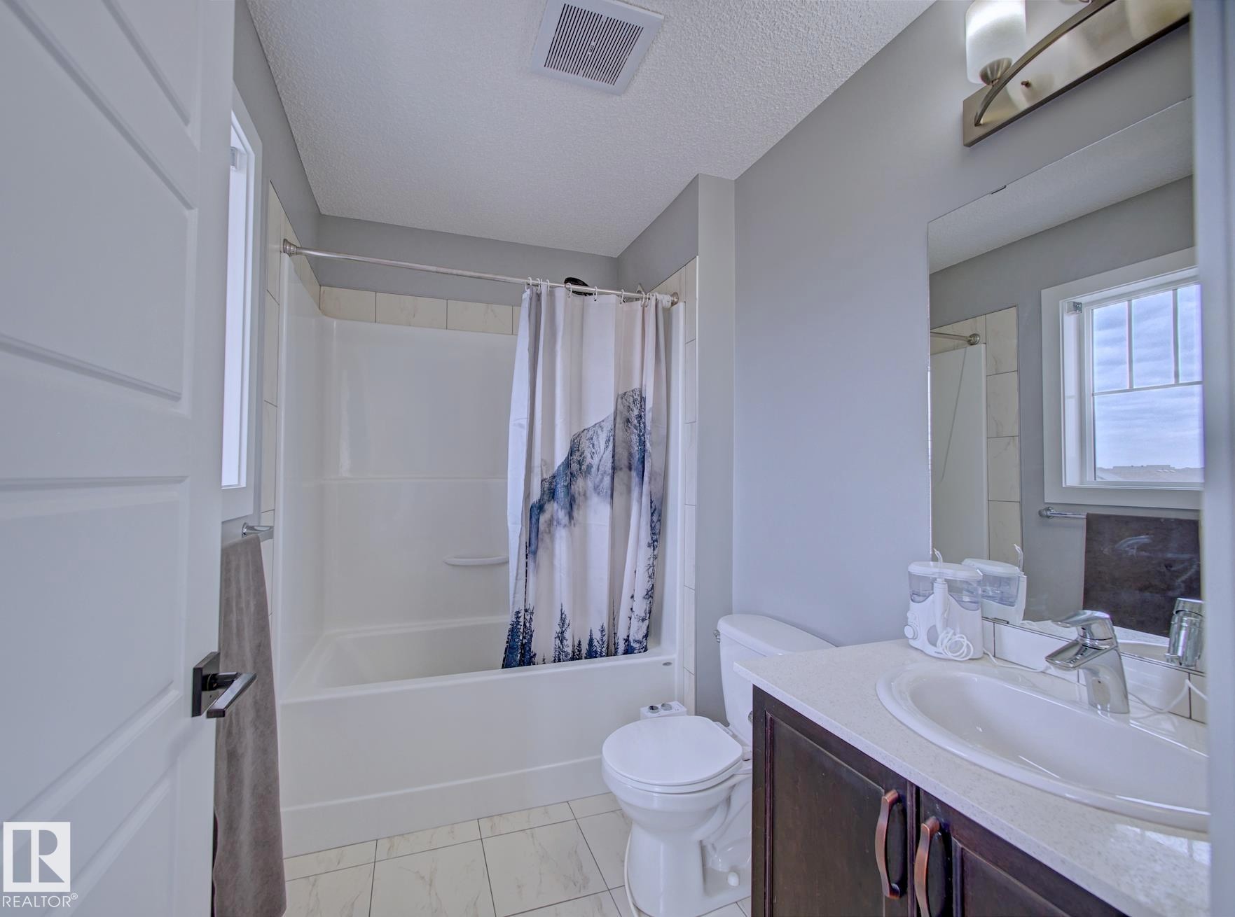 Full bathroom featuring a white tub/shower combination with tiled surround, a dark wood-finish vanity with an integrated sink, a large wall-mounted mirror, and tile flooring - 11 165 Cy Becker Boulevard, Edmonton, AB - Indoor Photo Showing Bathroom