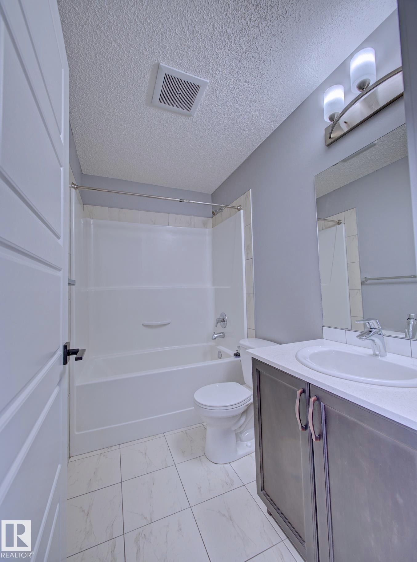 Upper 4PC Bathroom featuring a white bathtub with a tiled surround, a toilet, and a vanity with a white countertop and oval sink - 11 165 Cy Becker Boulevard, Edmonton, AB - Indoor Photo Showing Bathroom