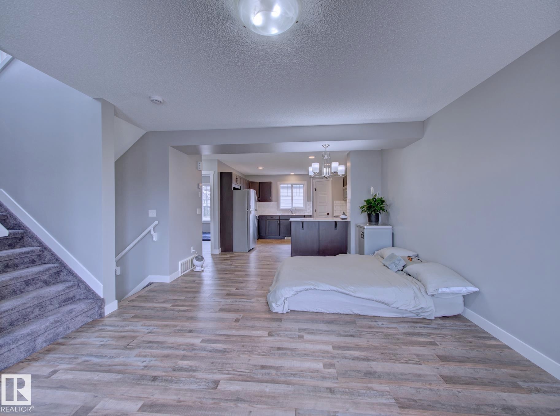 Open-concept living area with wood-finish flooring, a carpeted staircase, and neutral wall tones - 11 165 Cy Becker Boulevard, Edmonton, AB - Indoor