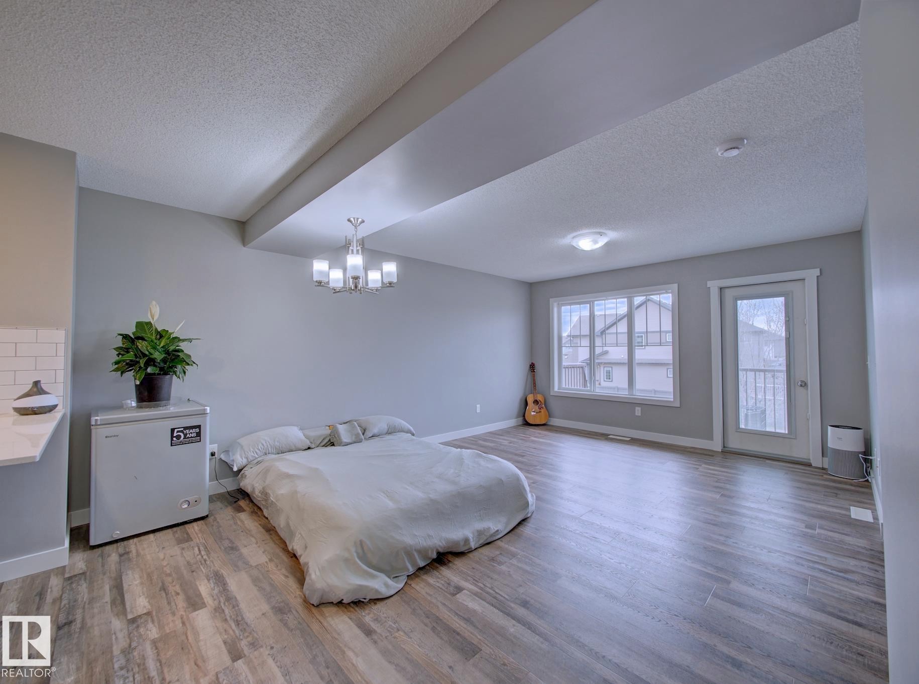 Spacious interior featuring wood-finish flooring, a contemporary chandelier, large windows with white trim, a built-in countertop with subway tile backsplash, and a glass-paneled exterior door - 11 165 Cy Becker Boulevard, Edmonton, AB - Indoor