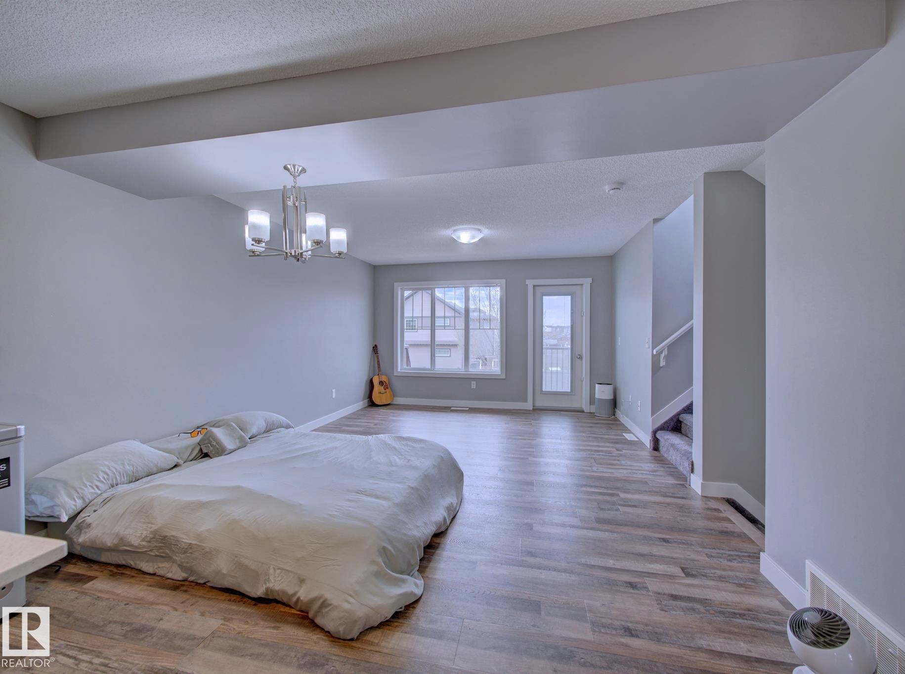 Spacious open-concept room featuring wood-finish flooring, light gray wall paint, and a modern chandelier - 11 165 Cy Becker Boulevard, Edmonton, AB - Indoor Photo Showing Bedroom