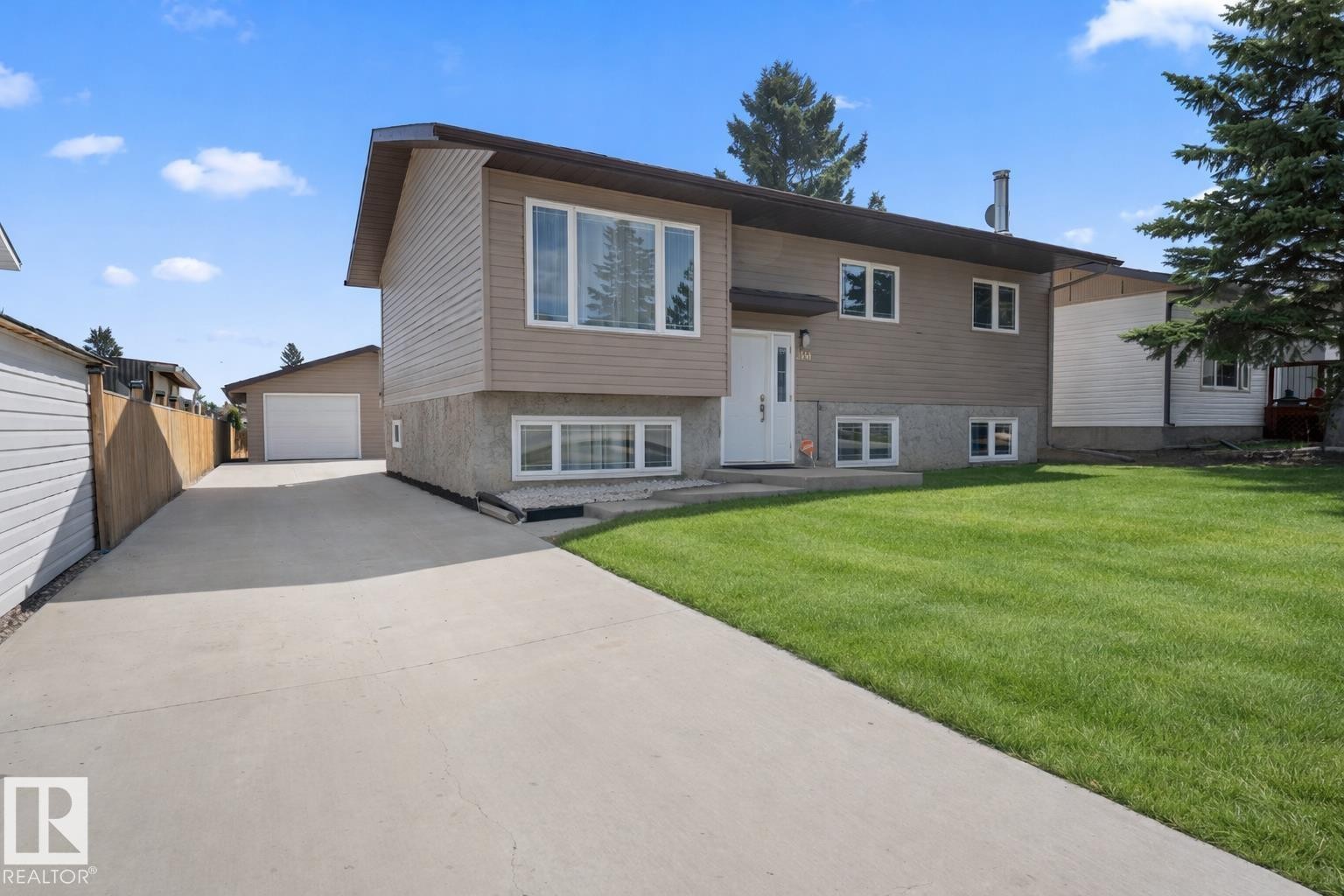 Split-level residence featuring a concrete driveway, a detached garage, and a lush green lawn - 1304 12 Street, Cold Lake, AB - Outdoor