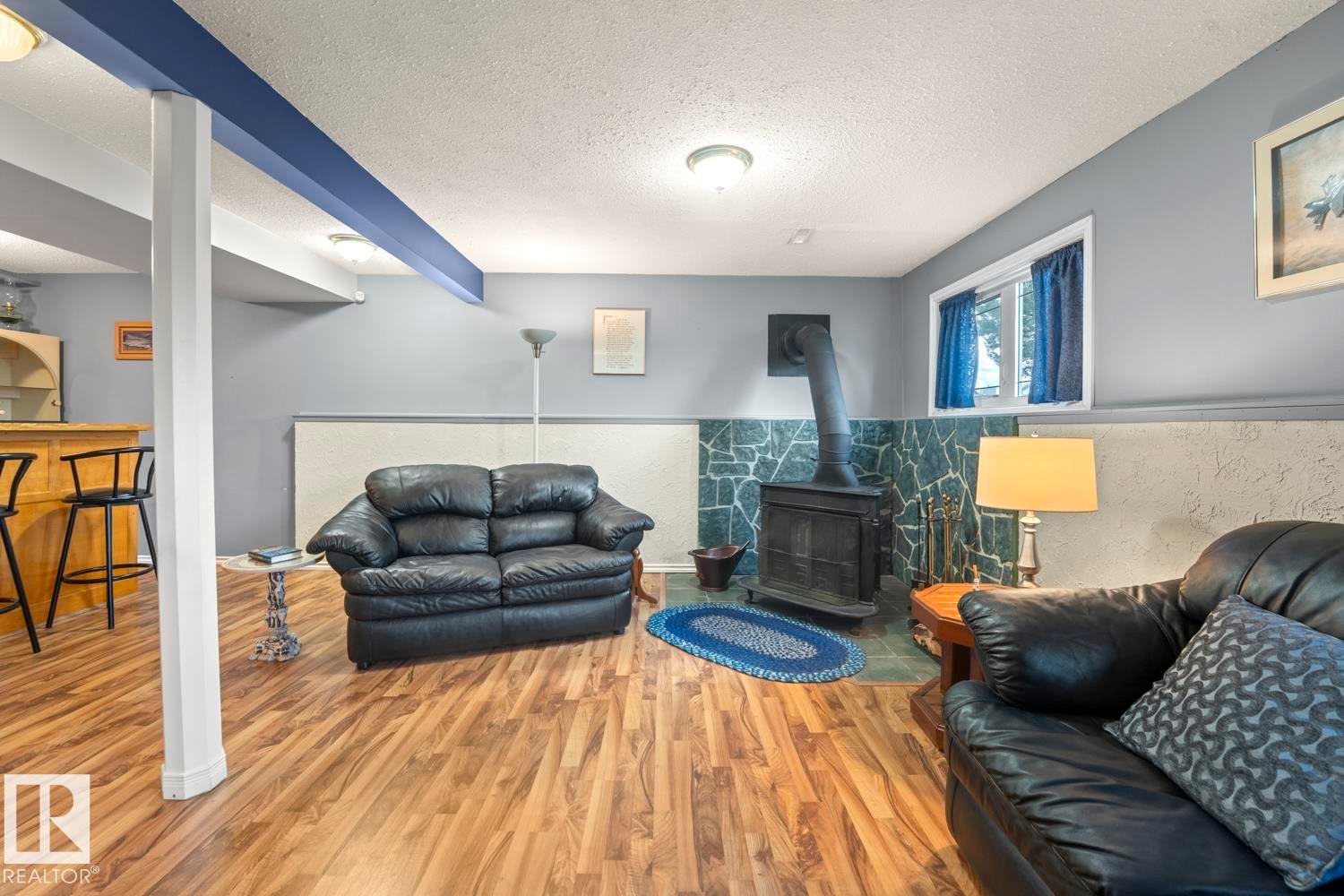 Wood-finish flooring throughout a spacious room featuring a built-in wet bar, a wood-burning stove with a stone surround, and recessed lighting - 1304 12 Street, Cold Lake, AB - Indoor Photo Showing Living Room